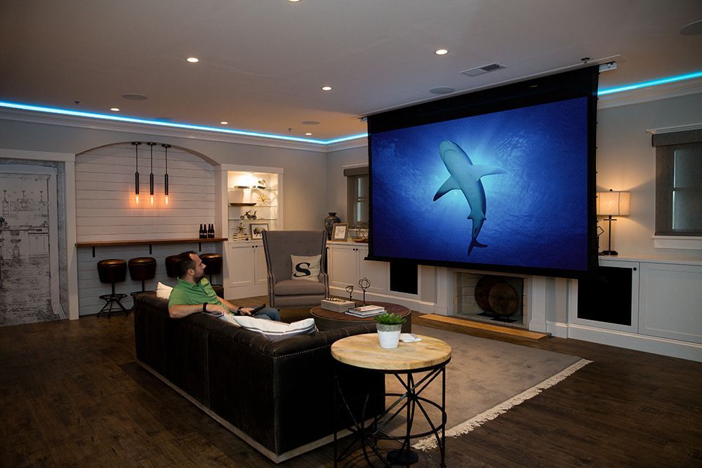 A man is sitting on a couch in front of a large screen in a living room.
