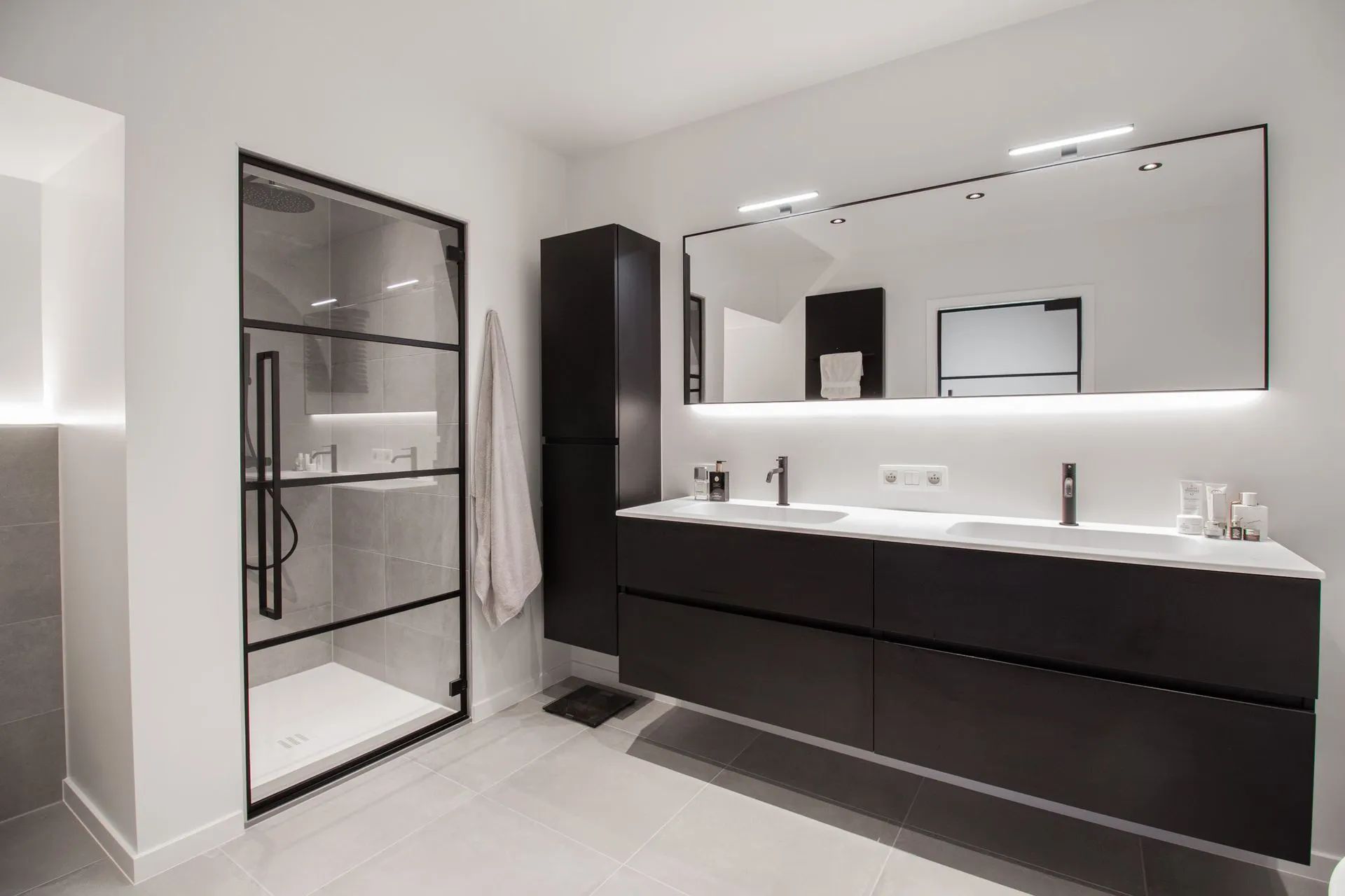 Moderne zwart-witte badkamer met douche, dubbele wastafel en hoge kast.