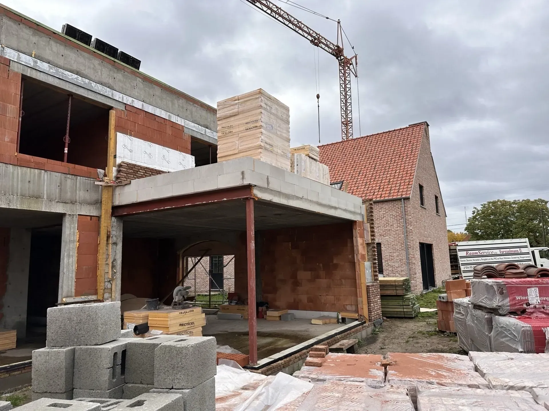 Bouwplaats: bakstenen gebouwen in aanbouw, kraan op de achtergrond, bewolkte lucht.