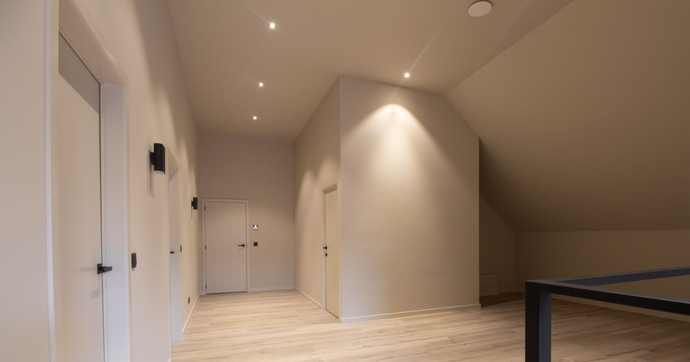 Ruime zolderkamer met houten balken, schuin wit plafond en lichte vloer met houtlook.