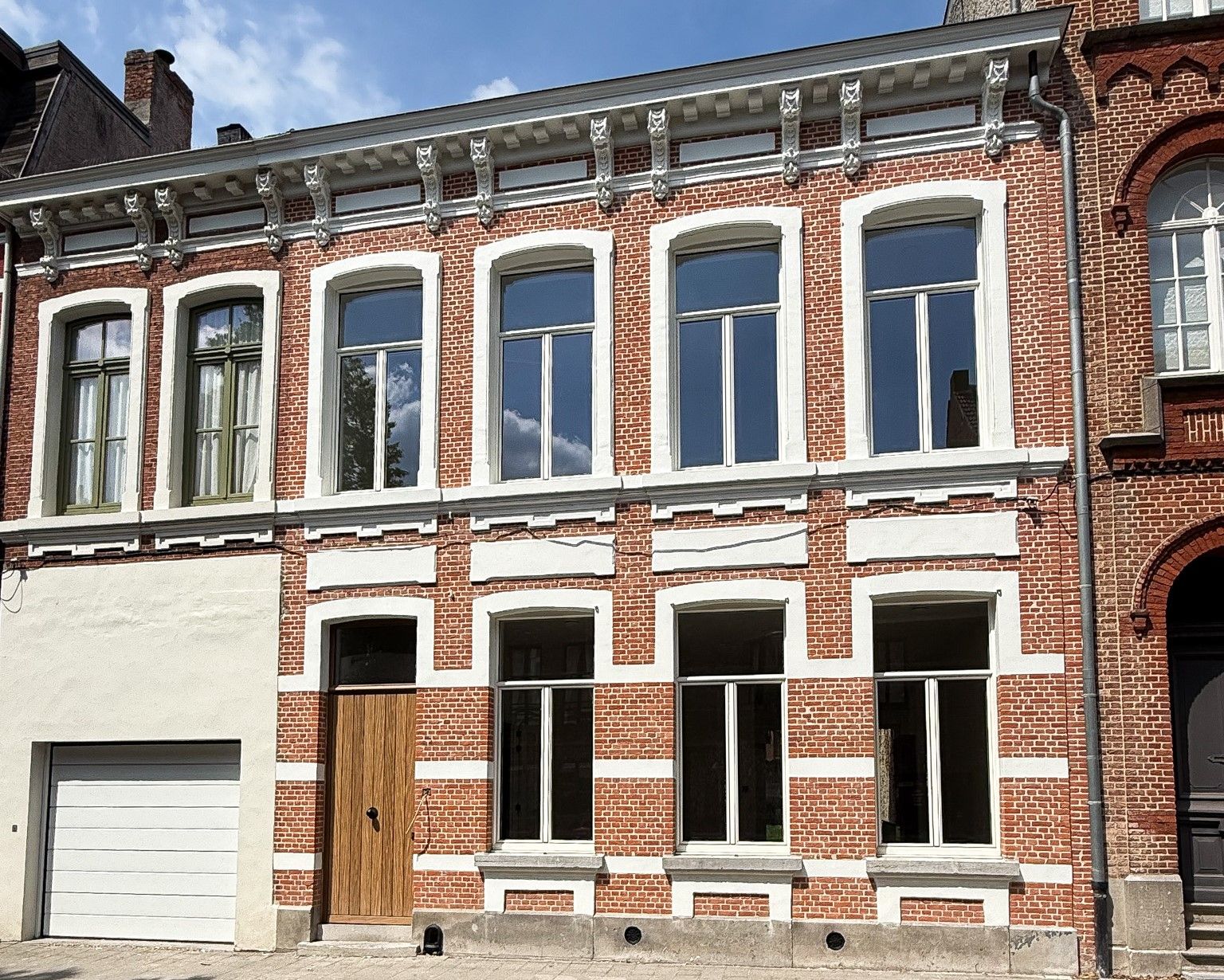 Bakstenen gebouw met witte raamkozijnen, meerdere ramen en een garagedeur.