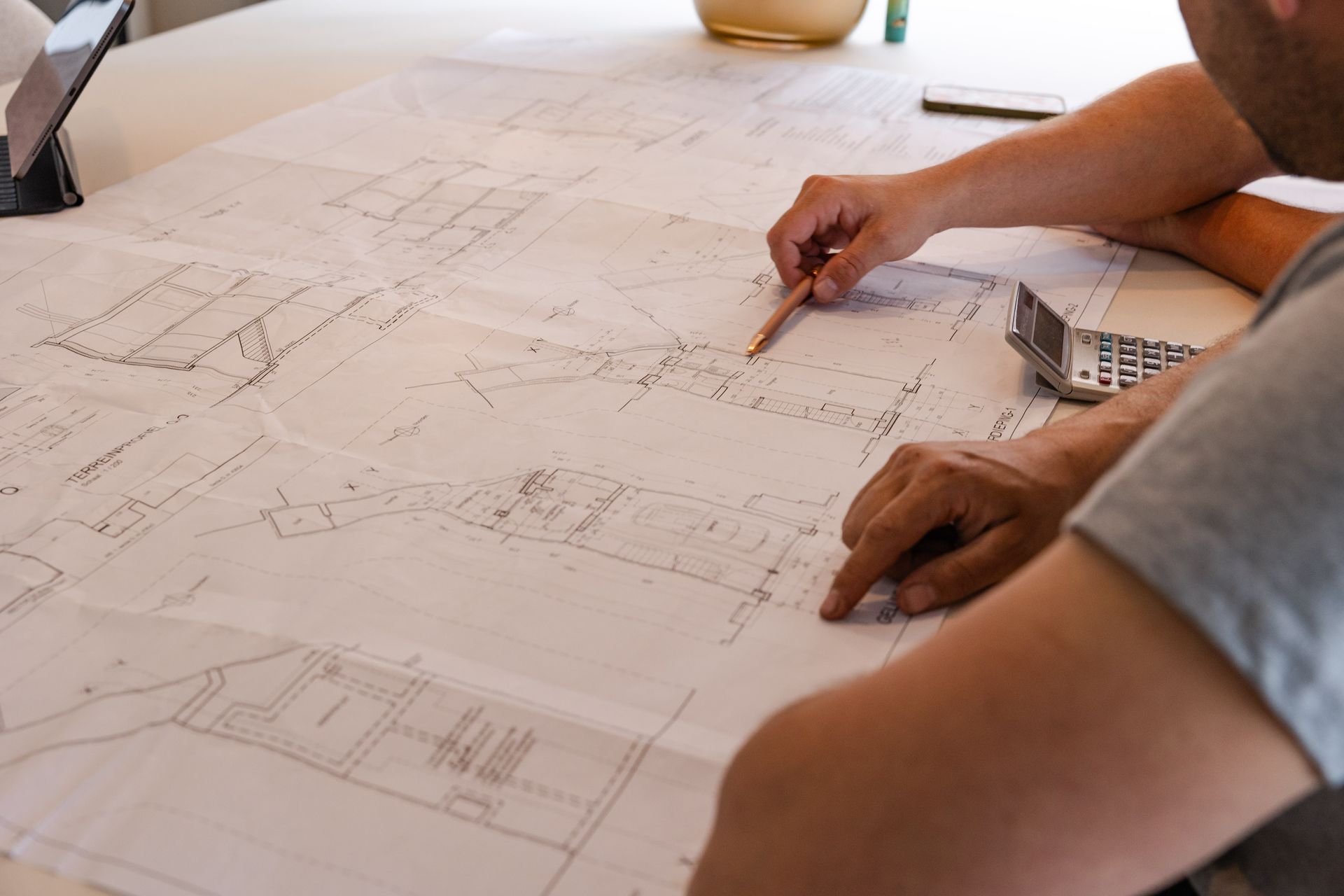 Persoon bekijkt architectuurtekeningen en wijst met potlood.