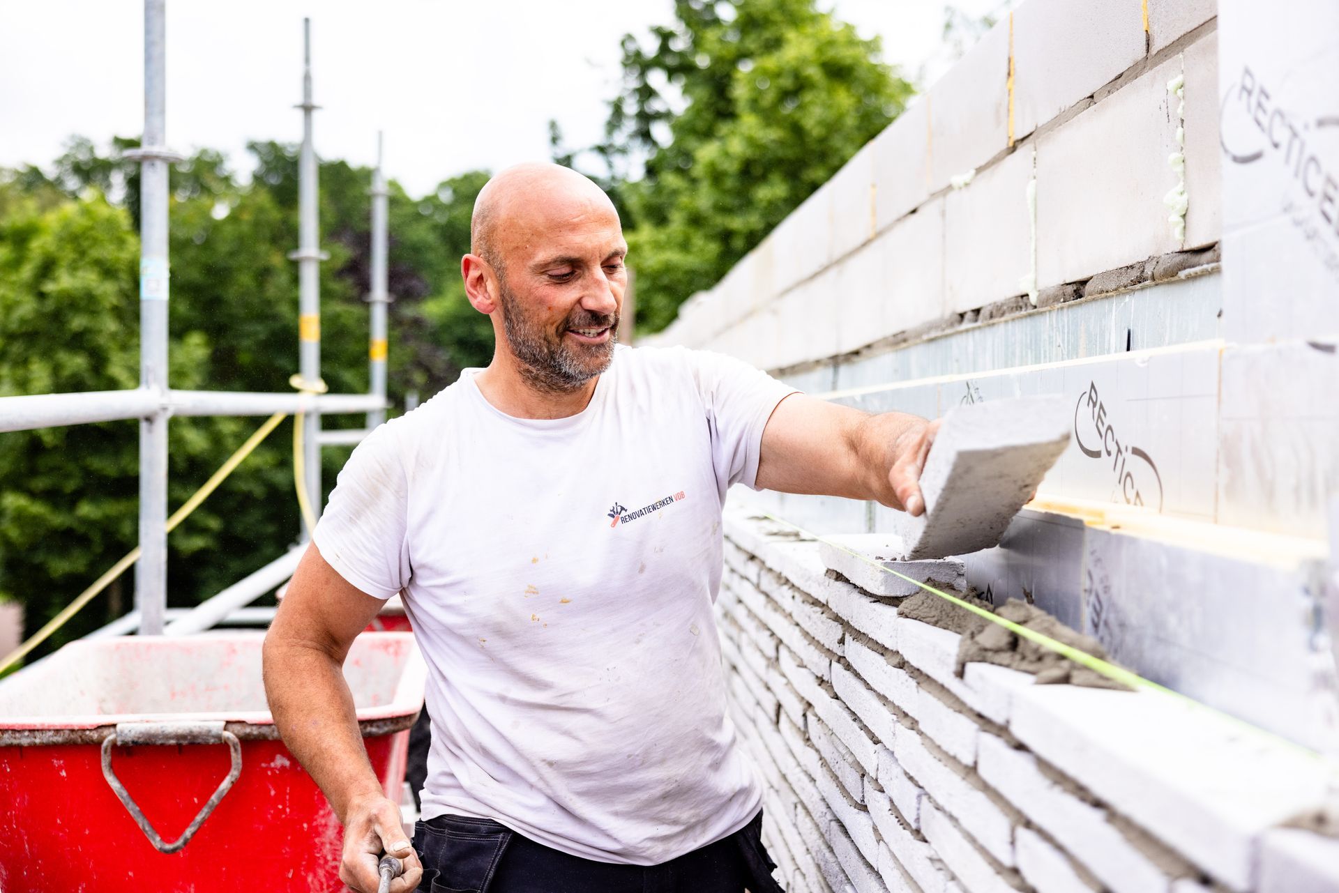 Een man legt stenen op een bouwplaats en gebruikt een troffel om mortel aan te brengen.
