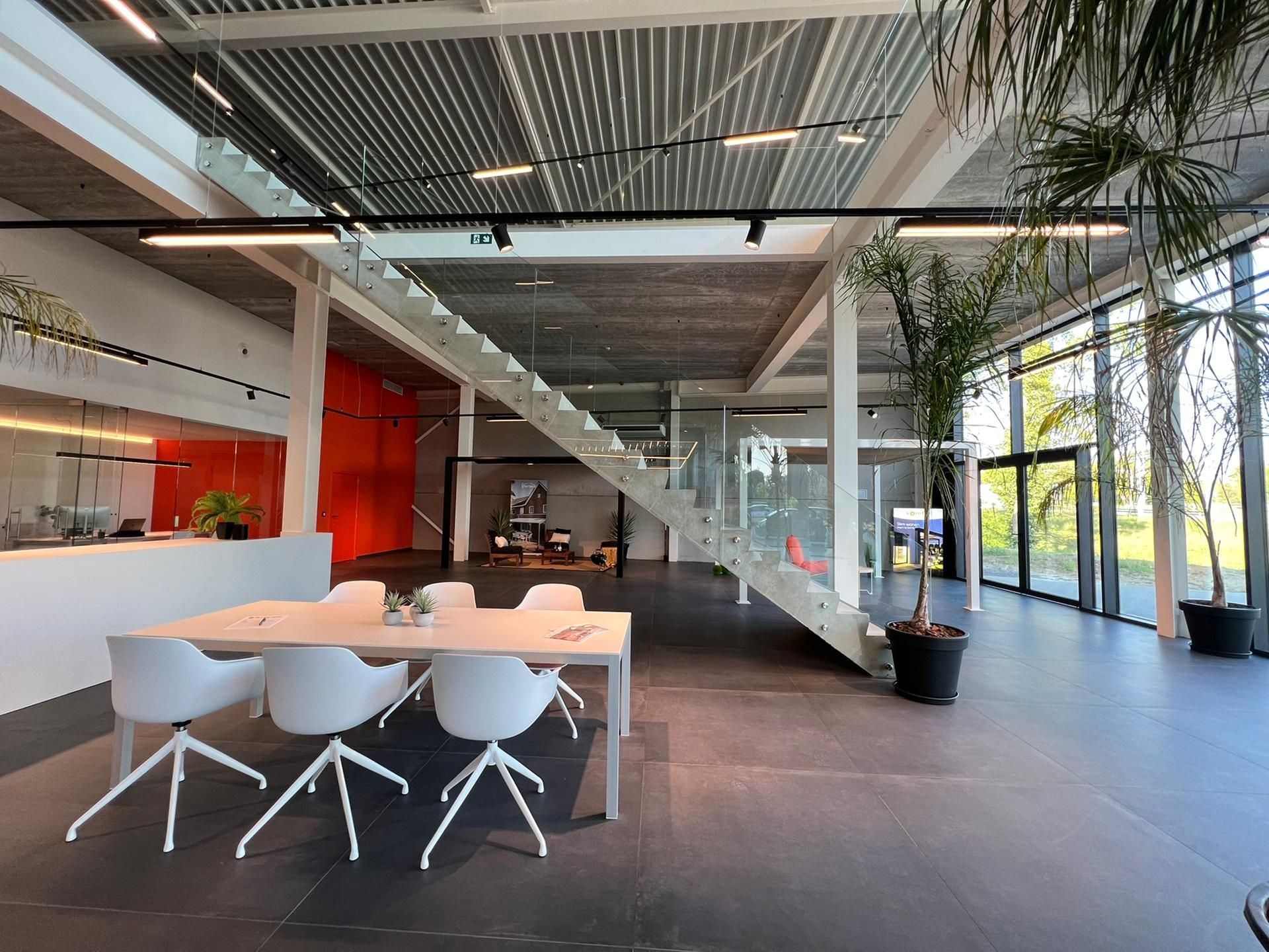 Moderne kantoorruimte met wit meubilair, een trap en potplanten. Grote ramen en heldere verlichting.