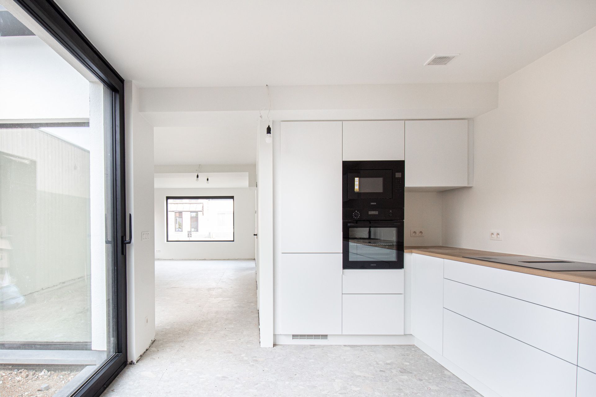 Moderne keuken met witte kasten, zwarte oven, houten aanrechtblad en grote glazen schuifdeur.