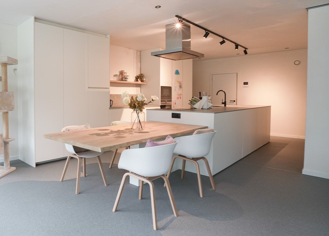 Moderne witte keuken met kookeiland, houten vloer, deur naar buiten en een kruk.