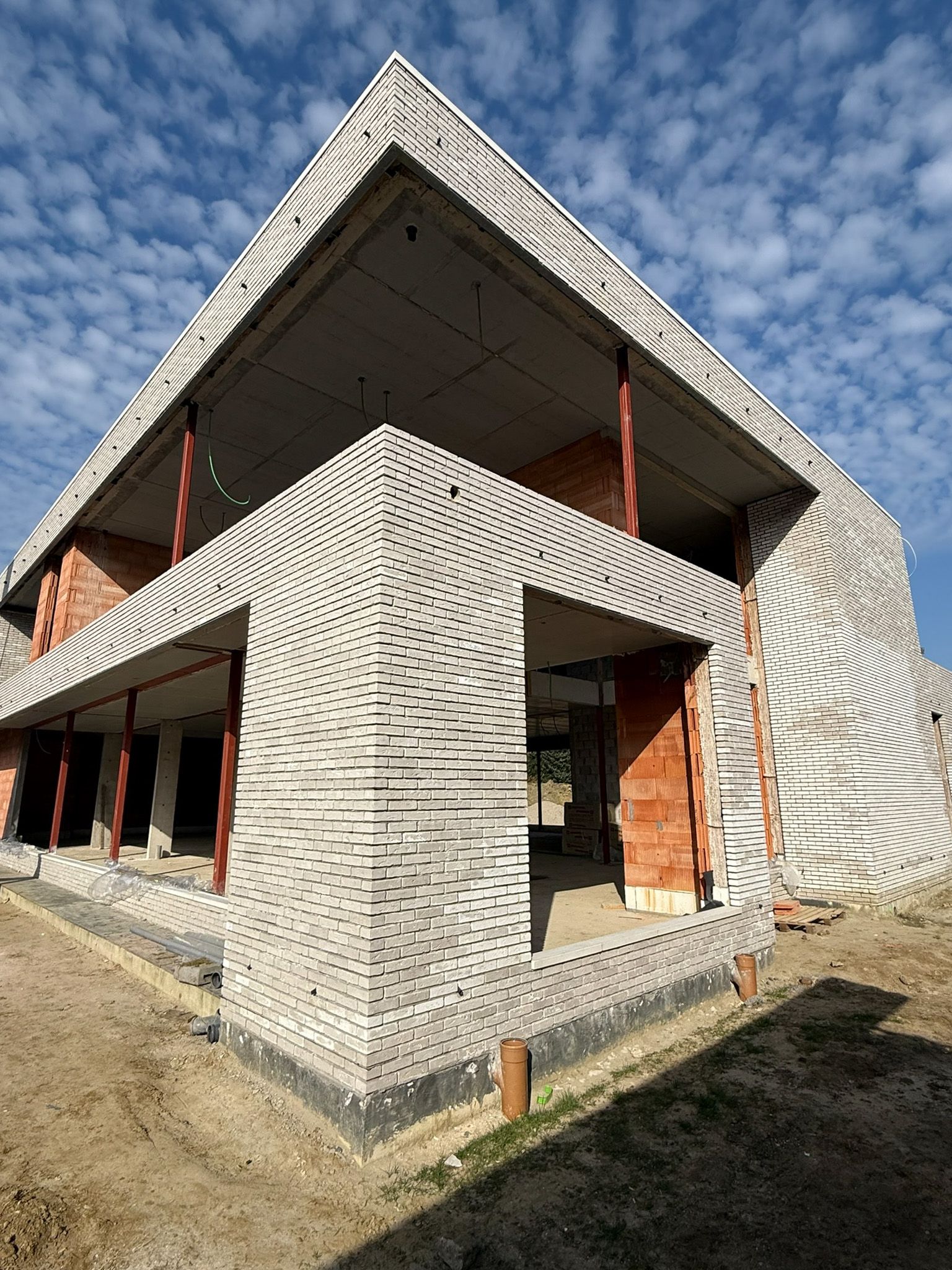 Modern gebouw met twee verdiepingen in aanbouw, met een gevel in grijs en wit met een textuur tegen een blauwe lucht.