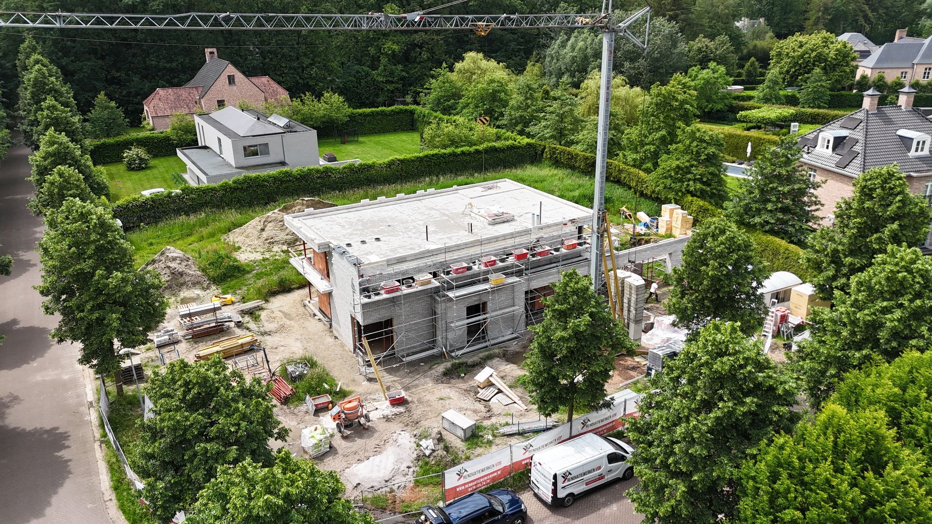 Bouw van een huis met meerdere verdiepingen, omgeven door bomen, met een kraan erboven, in een woonwijk.