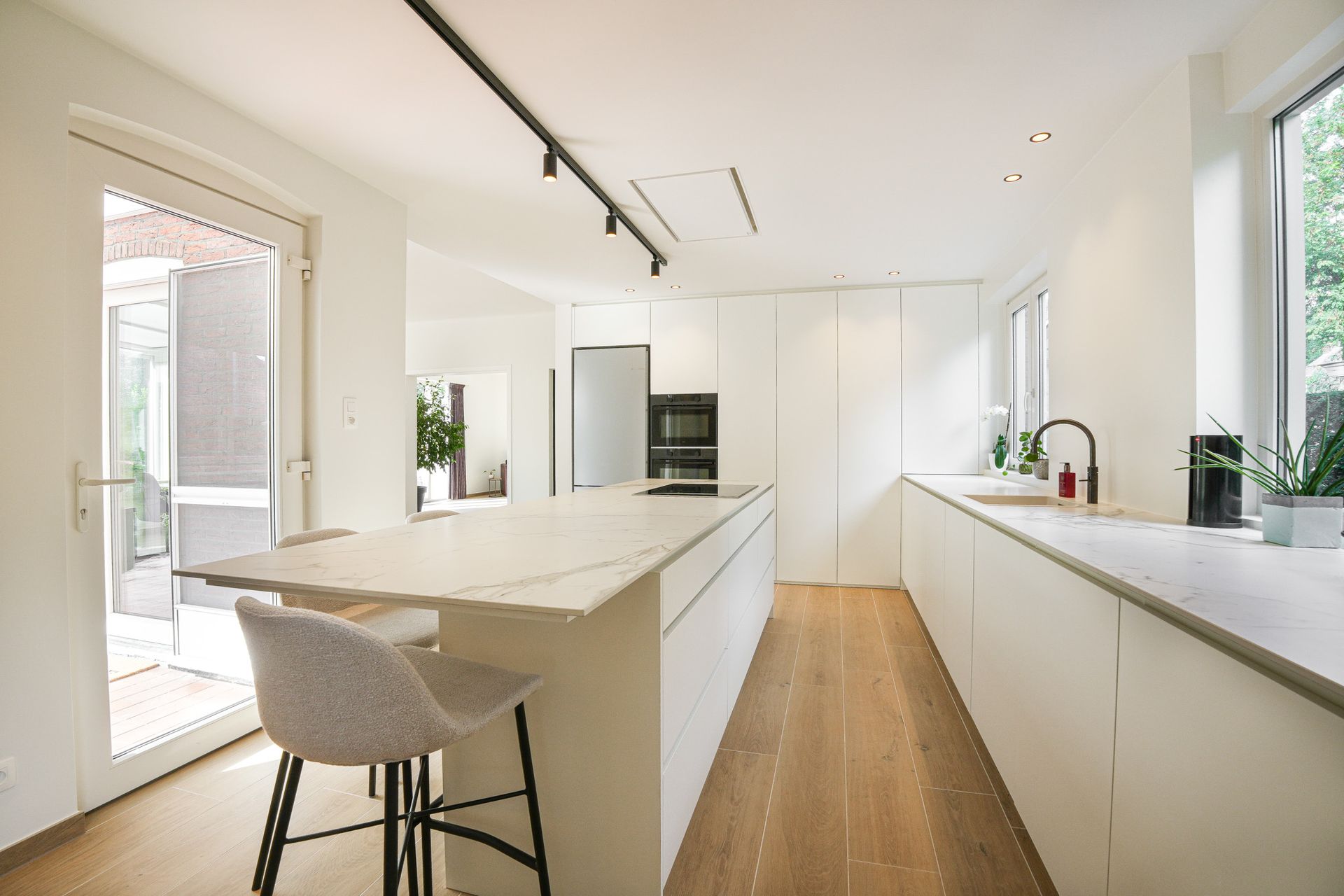 Moderne keuken met witte kasten, kookeiland, houten tafel en witte stoelen.