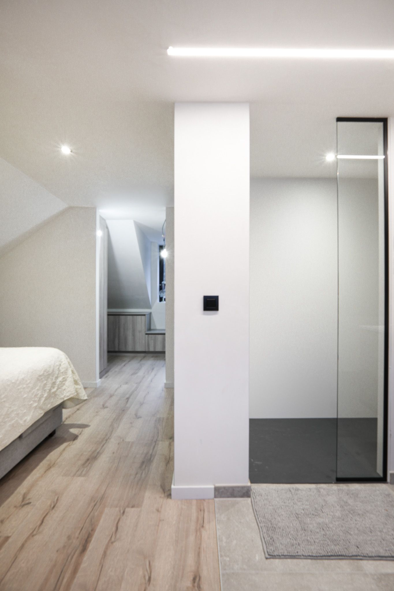 Moderne slaapkamer met lichte houten vloeren, witte muren en een douche met glazen wanden.