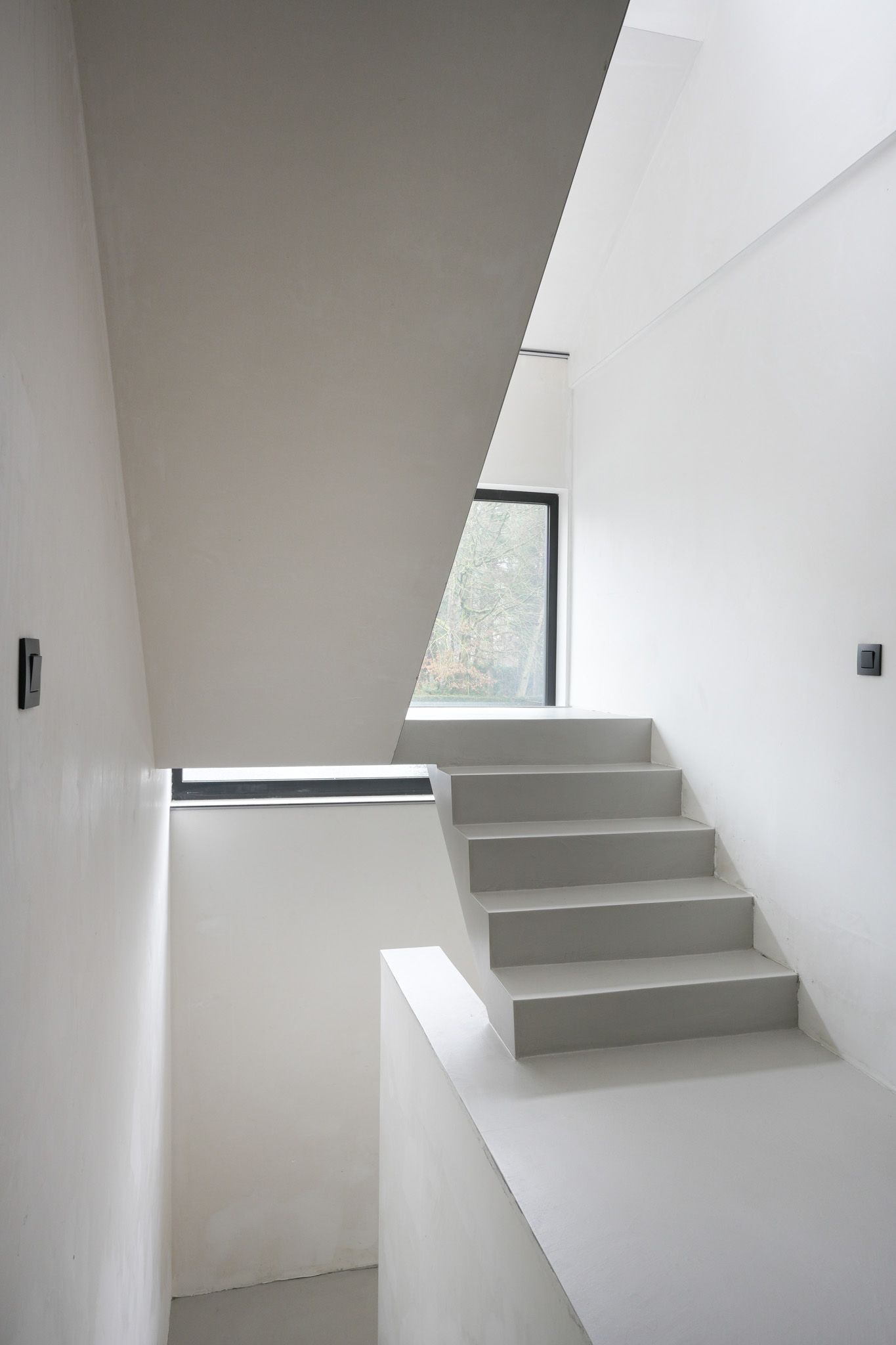Witte trap leidt naar een raam, sober interieur.