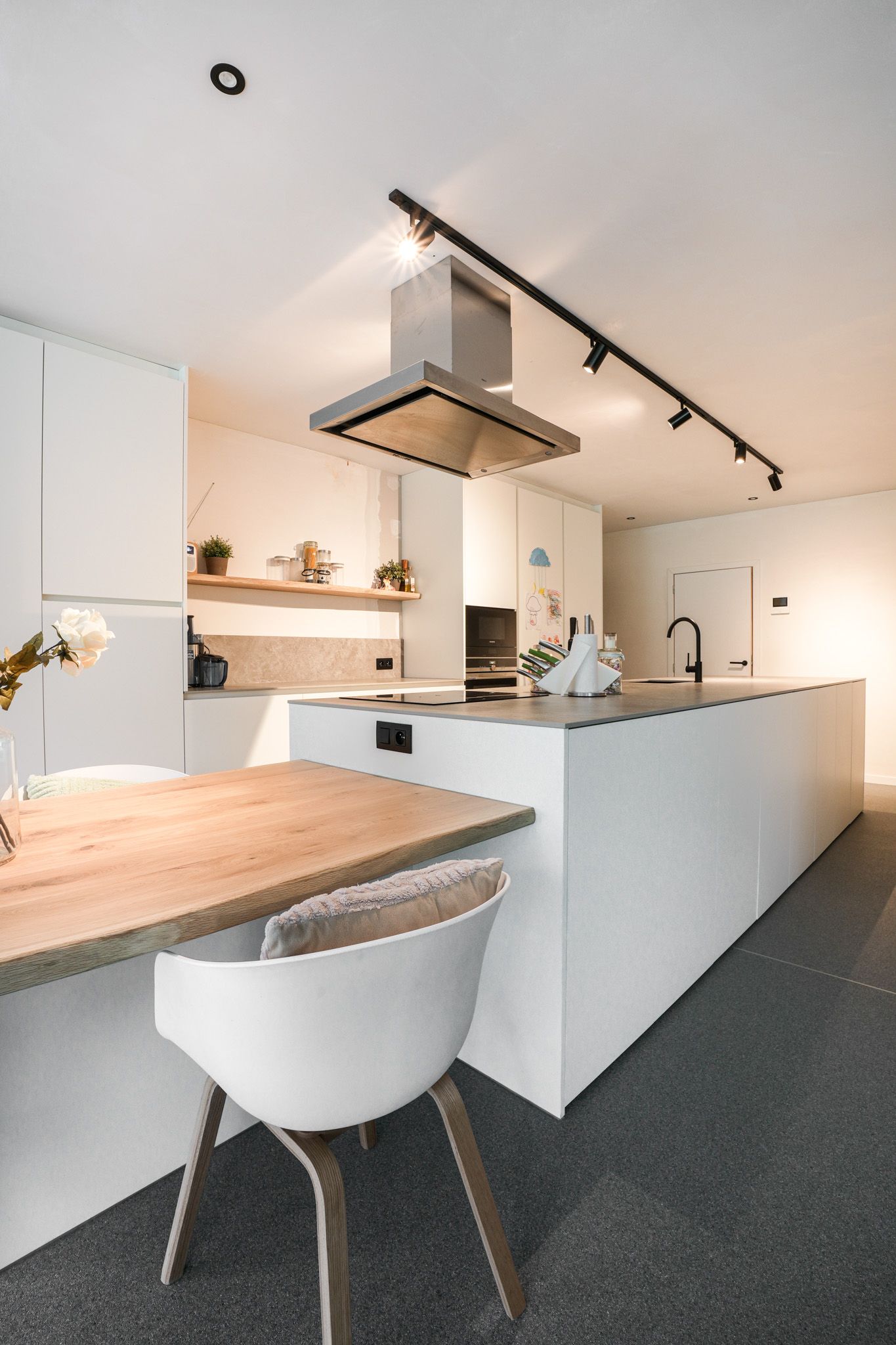 Moderne witte keuken met kookeiland, eettafel en plafondverlichting.