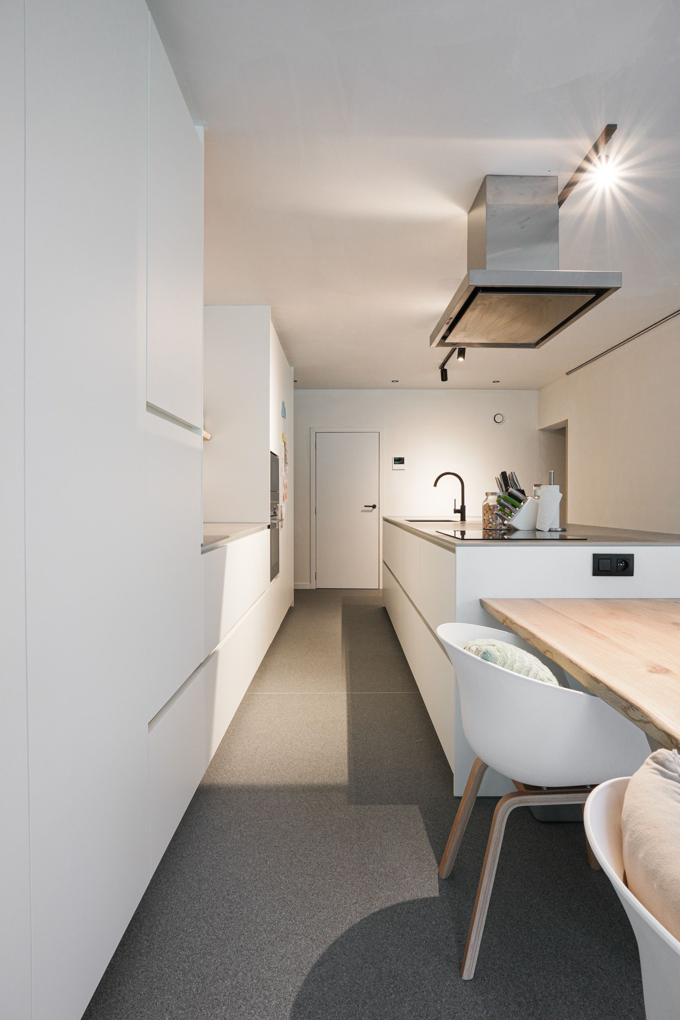 Moderne witte keuken met lang kookeiland, kasten, eettafel en stoelen.