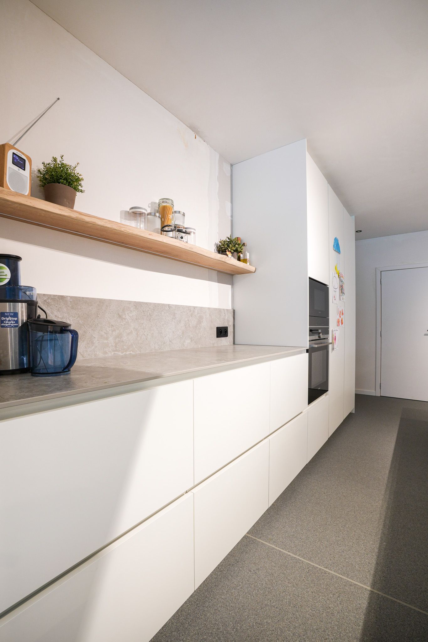 Moderne witte keuken met lichte werkbladen en houten planken.