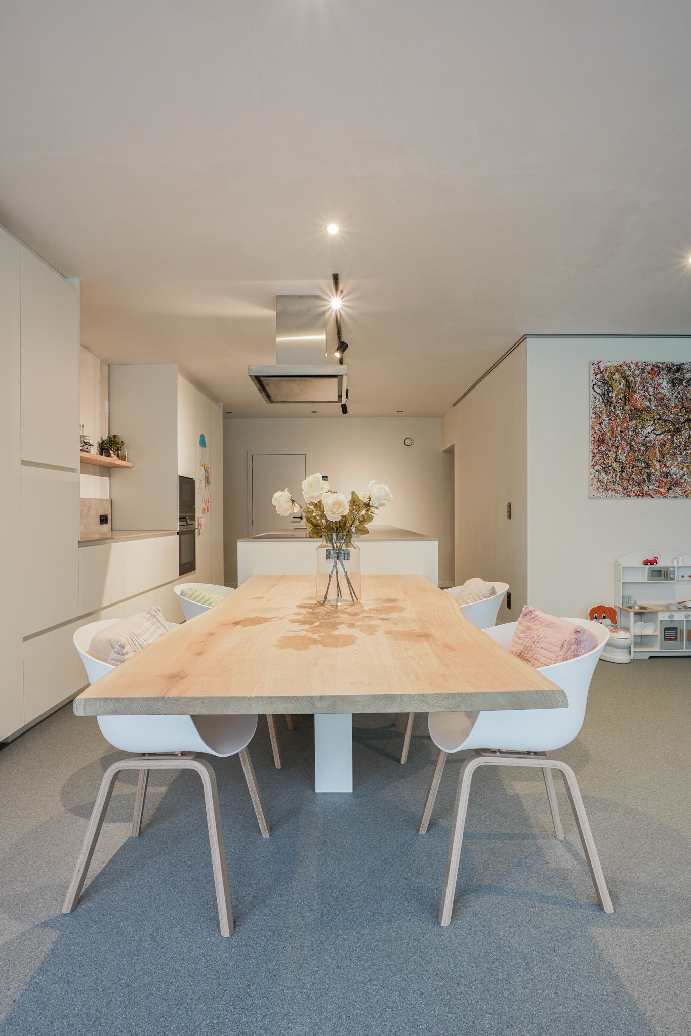 Eetkamer met een grote houten tafel, witte stoelen en minimalistische inrichting.
