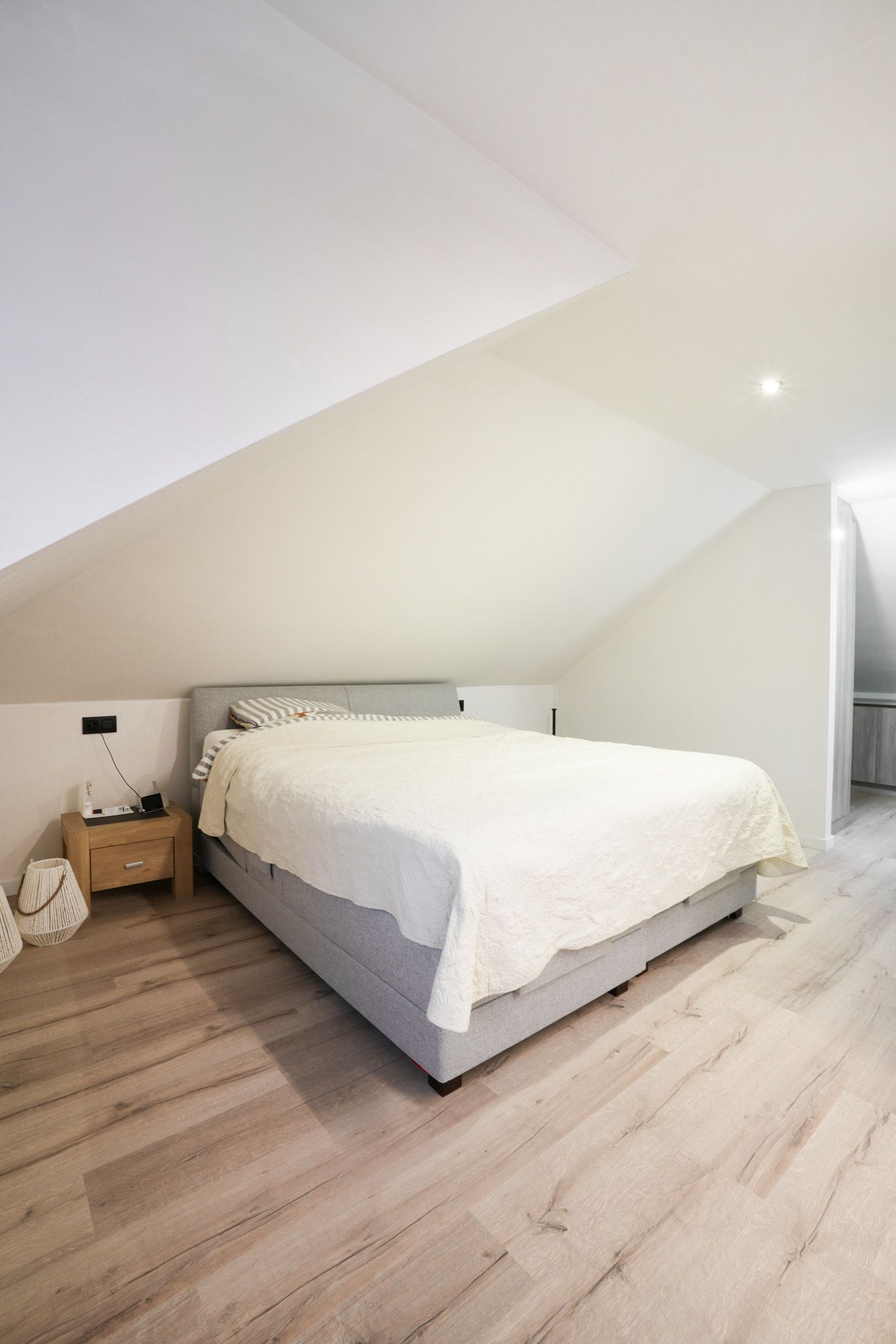 Slaapkamer met een bed, nachtkastje en een houten vloer in een kamer met een schuin plafond.