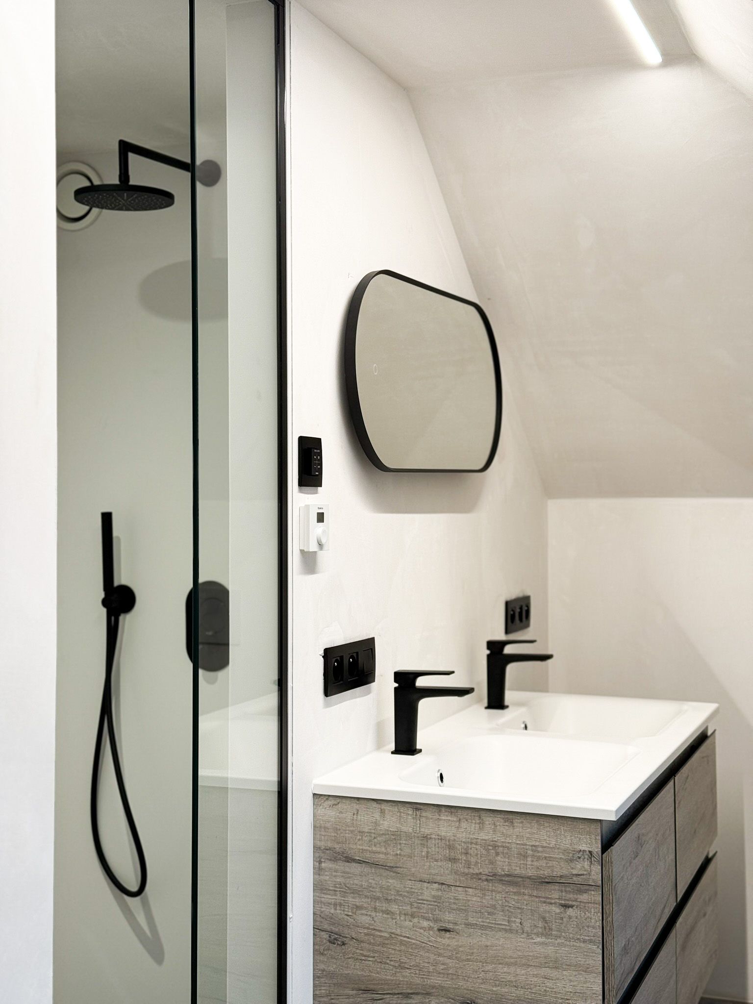 Moderne badkamer met douche, wastafel en zwarte armaturen. Witte muren en een kast met natuursteenlook.