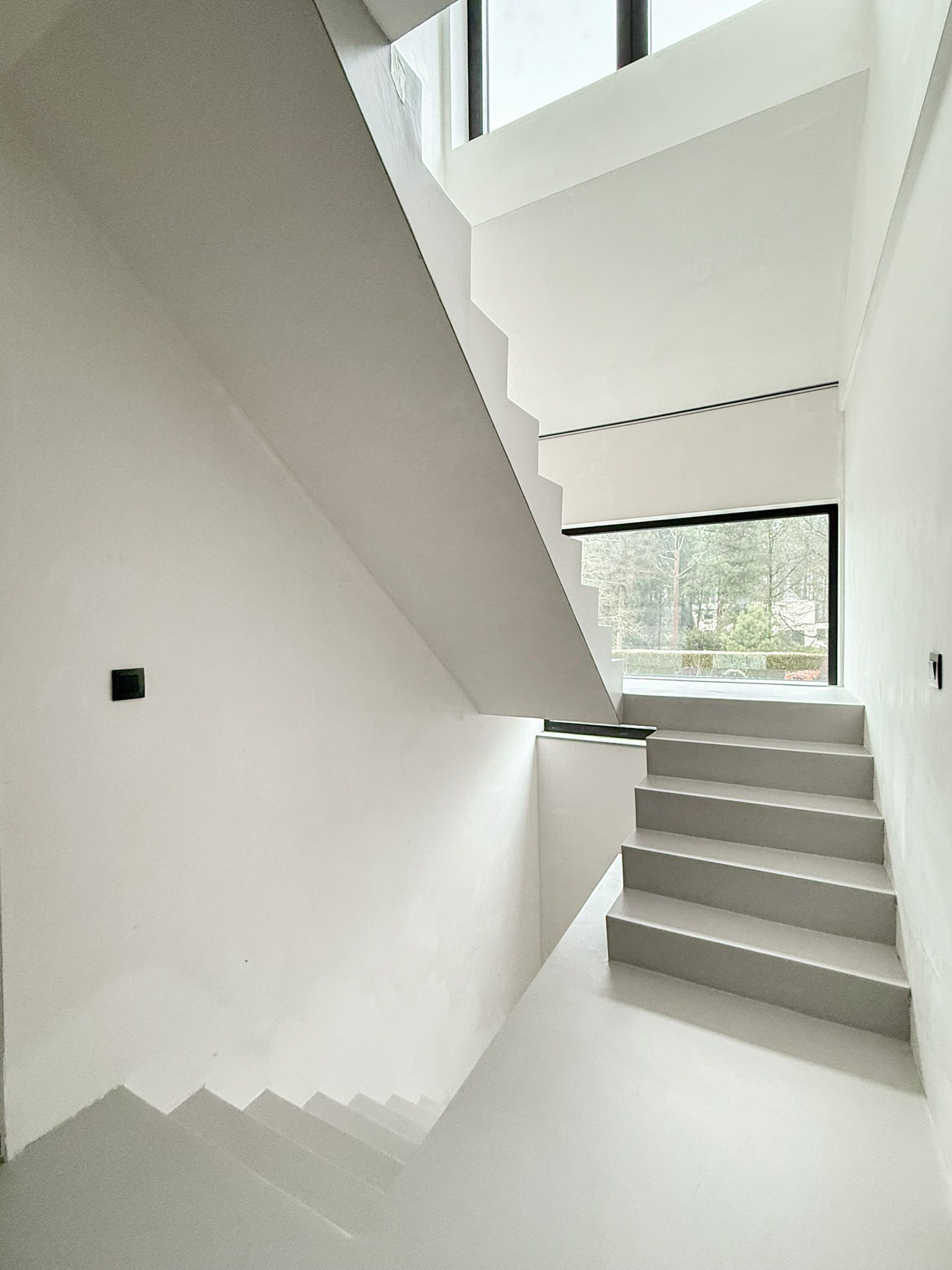 Modern interieur met een betonnen trap en witte muren. Zonlicht stroomt door een raam.