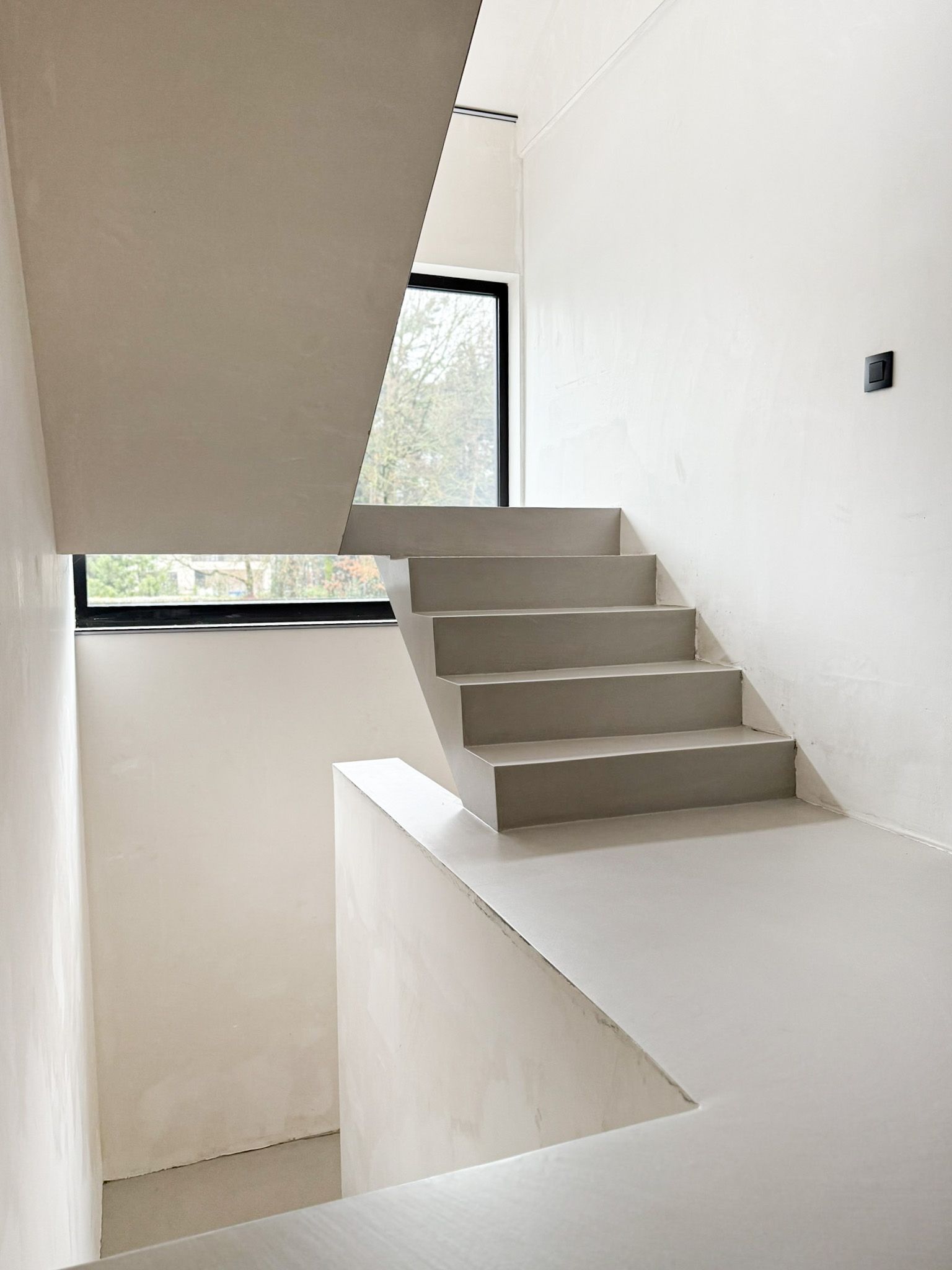 Betonnen trap met geometrisch ontwerp, raam en witte muren.