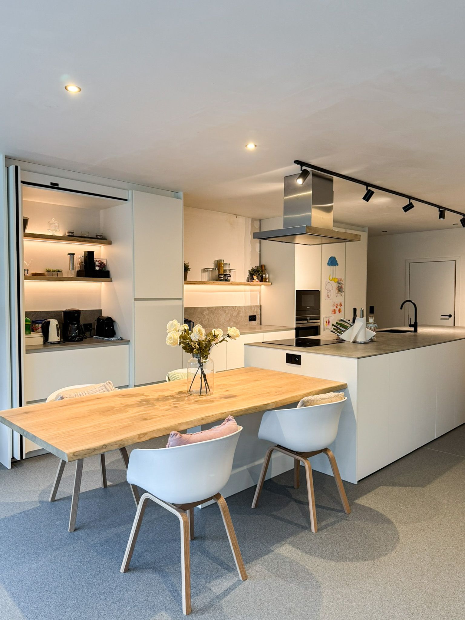 Moderne keuken met een lichte houten eettafel en witte stoelen, kookeiland en kasten.