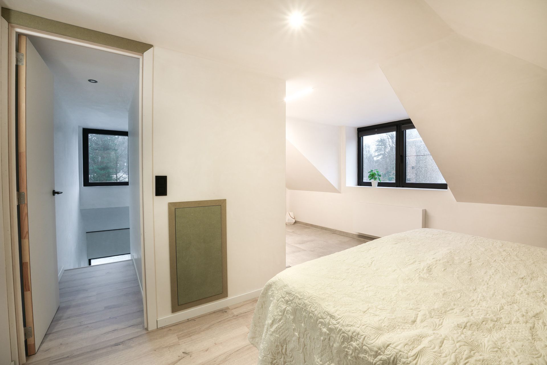 Slaapkamer met bed, deur naar de gang en ramen. Witte muren, natuurlijk licht.