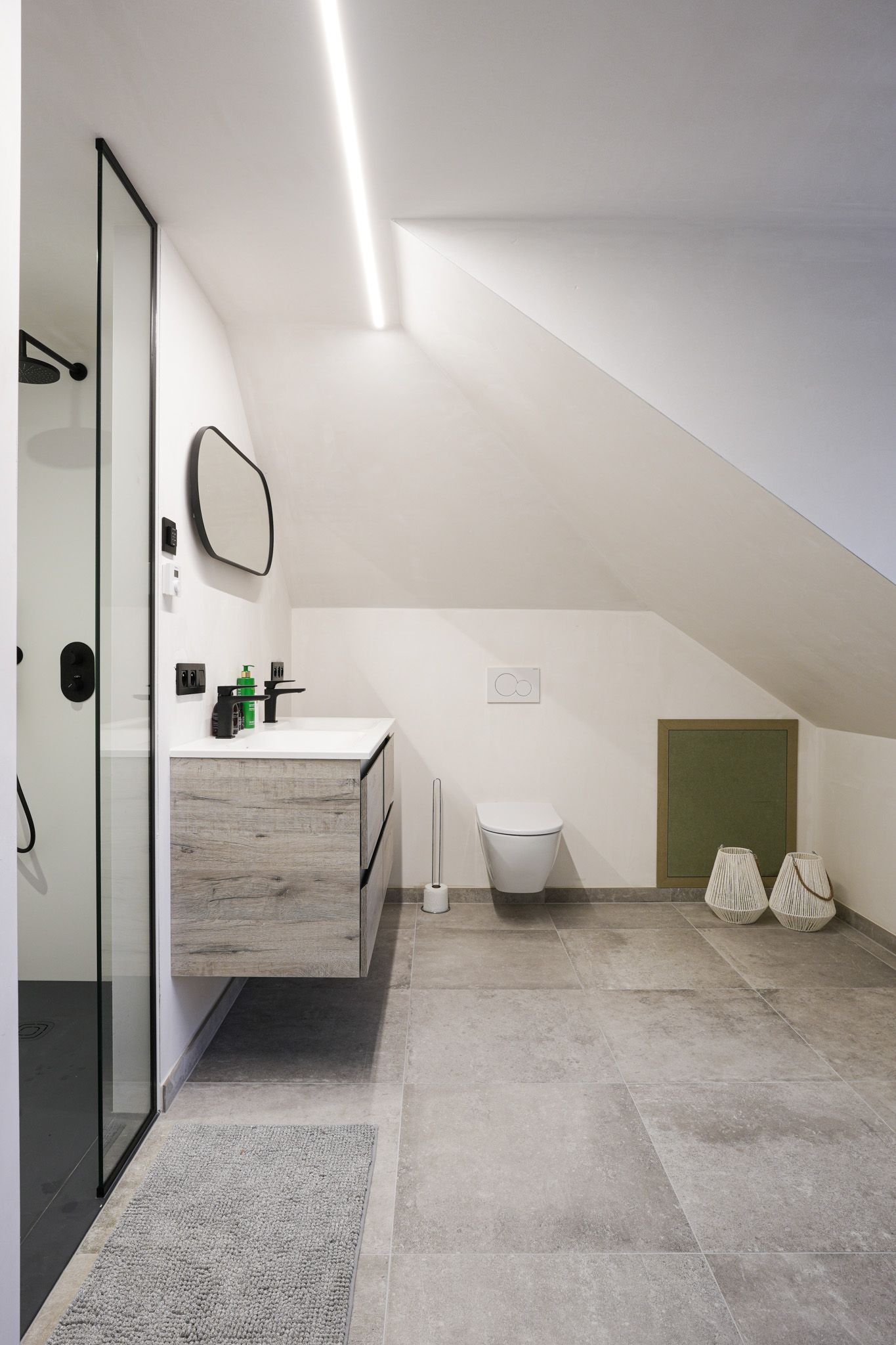 Moderne badkamer met douche, wastafel, toilet en schuin plafond. Grijze vloeren, witte muren en groene accenten.