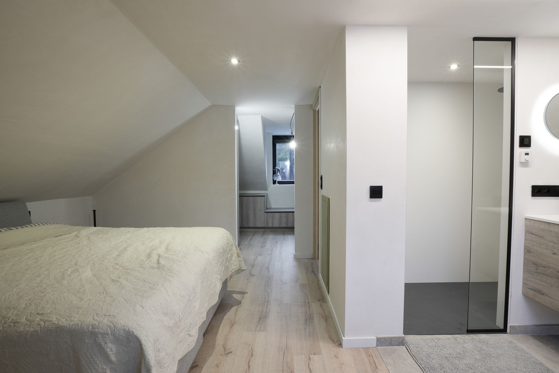 Slaapkamer en badkamer met schuine plafonds, lichte houten vloeren en moderne armaturen.