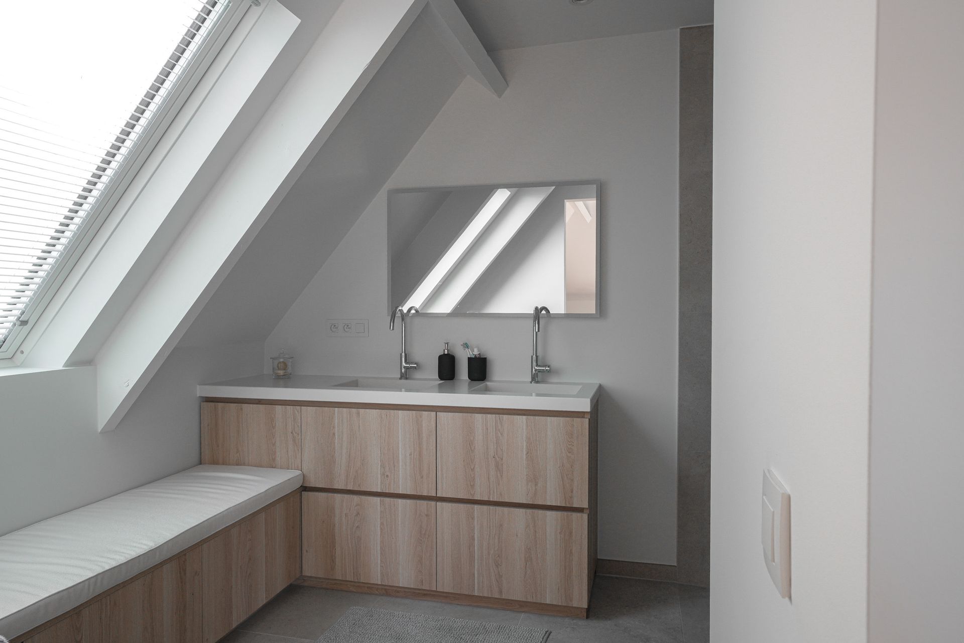 Badkamer met dakraam, lichthouten wastafelmeubel met dubbele wastafels, grote spiegel en een ingebouwde bank.
