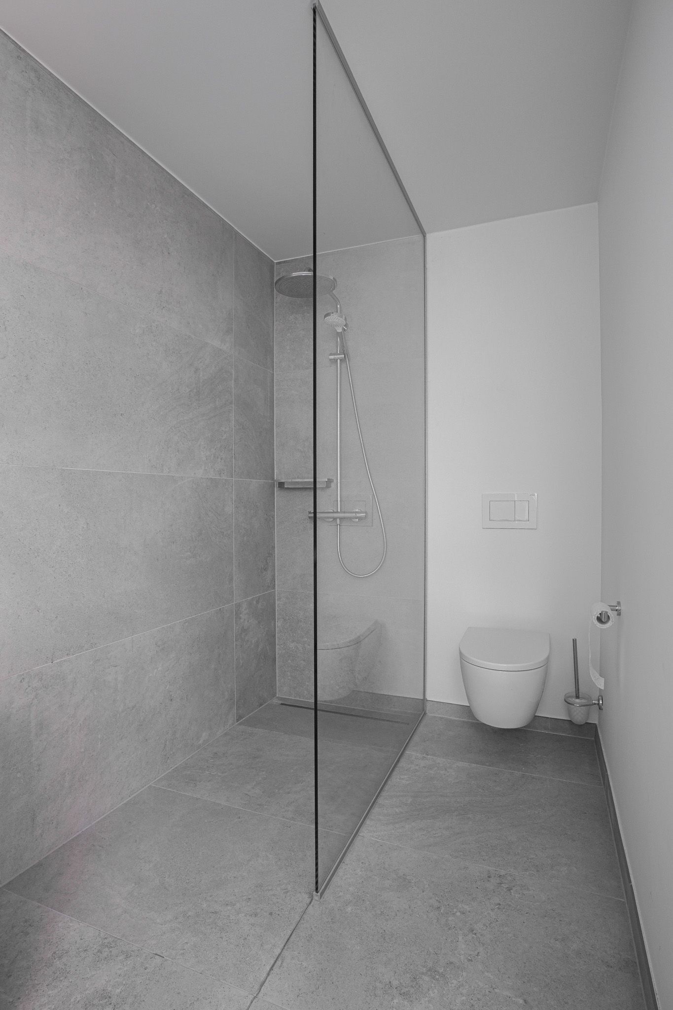 Moderne badkamer met glazen douche en toilet. Betonnen muren en vloer in grijs- en wittinten.