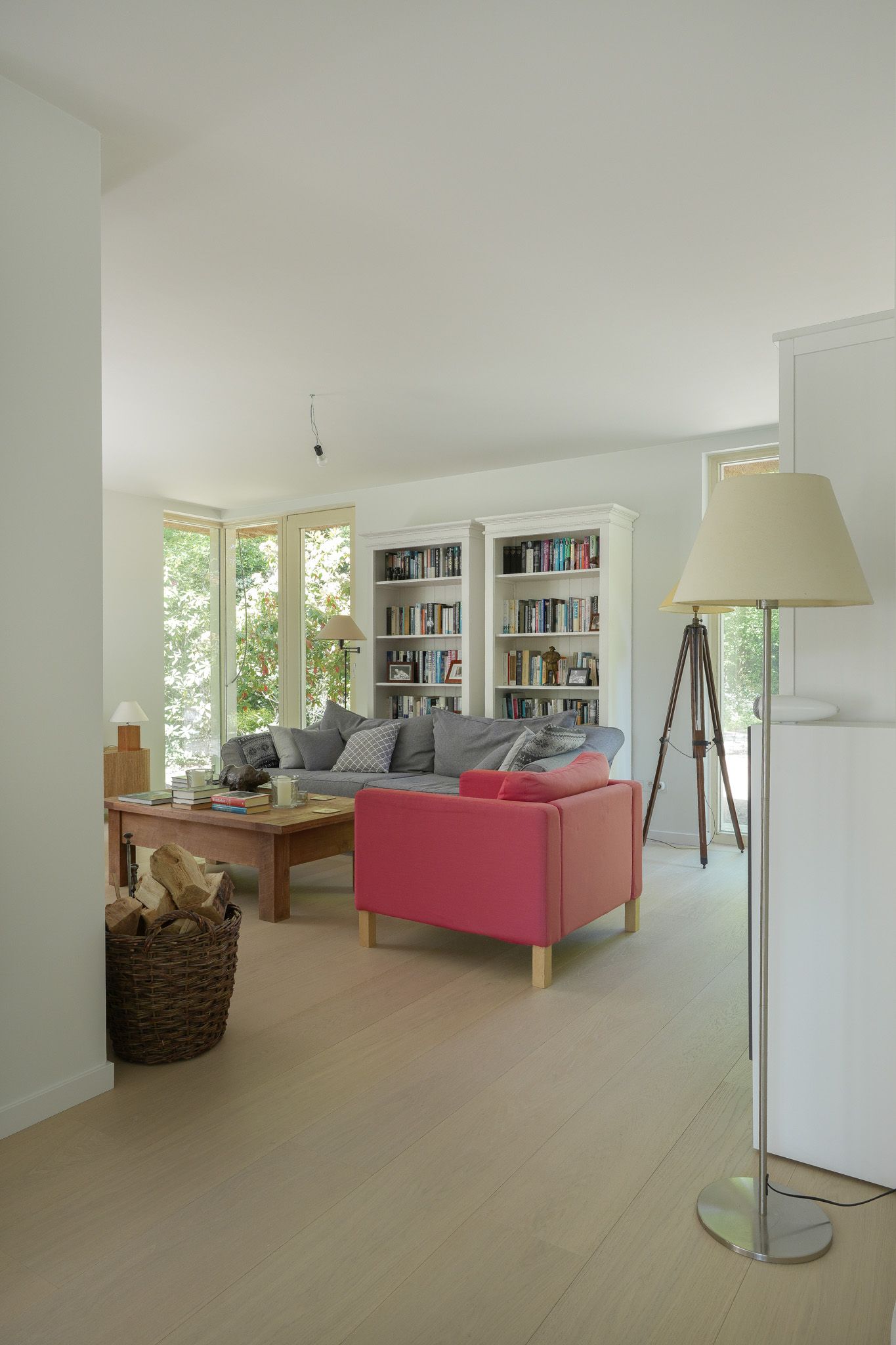 Woonkamer met roze bank, boekenkast, houten vloer en hoge lamp.