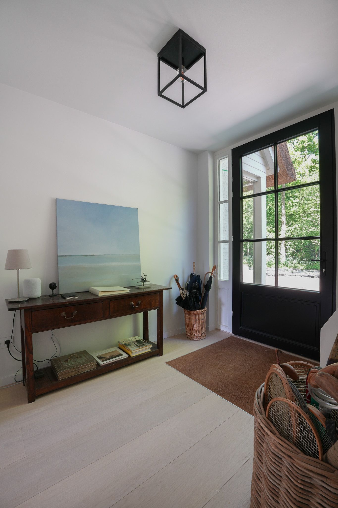 Entree met een donkere deur, witte muren en een houten tafel met een schilderij.