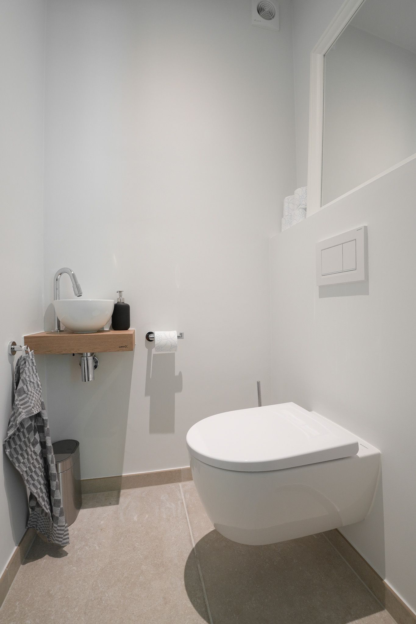 Kleine, minimalistische witte badkamer met zwevend toilet en wastafel, houten plank en handdoek.