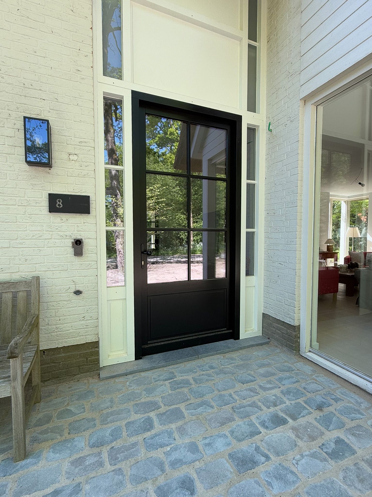 Zwarte deur met glazen panelen en zijramen, op een terras van grijze steen.