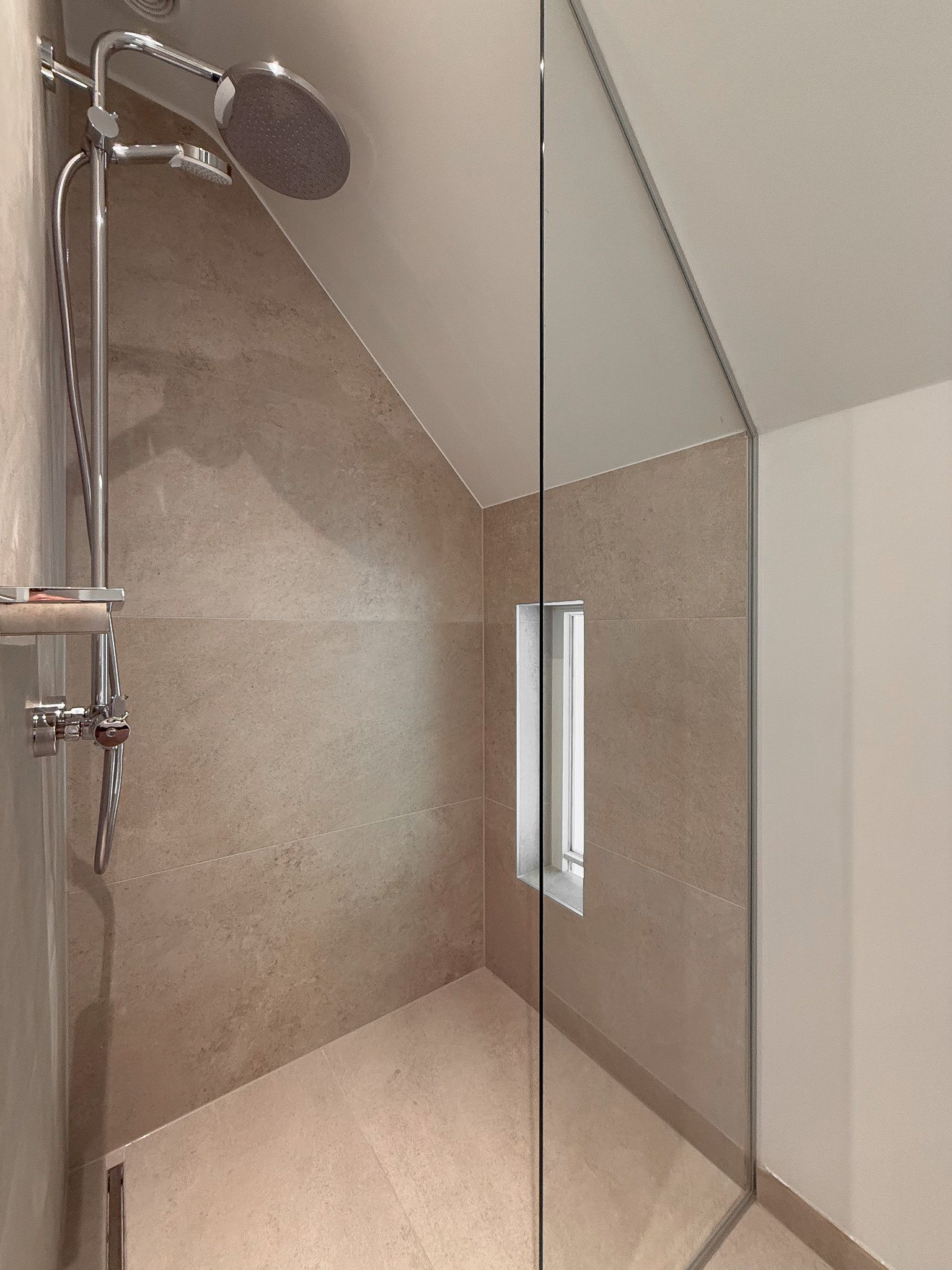 Douche met beige tegels, glazen deur en regendouchekop.