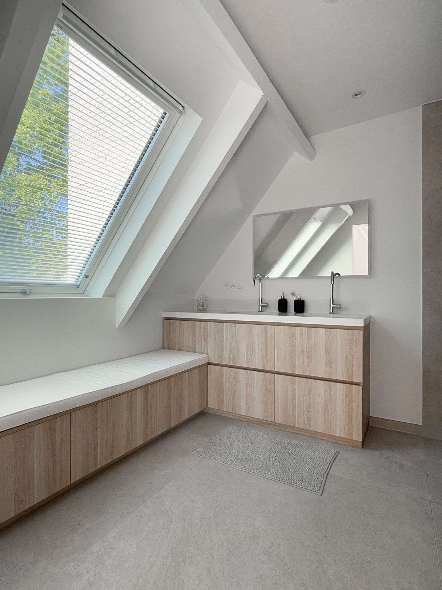 Moderne badkamer met schuin dakraam, houten wastafelmeubel en lichtgrijze muren en vloer.