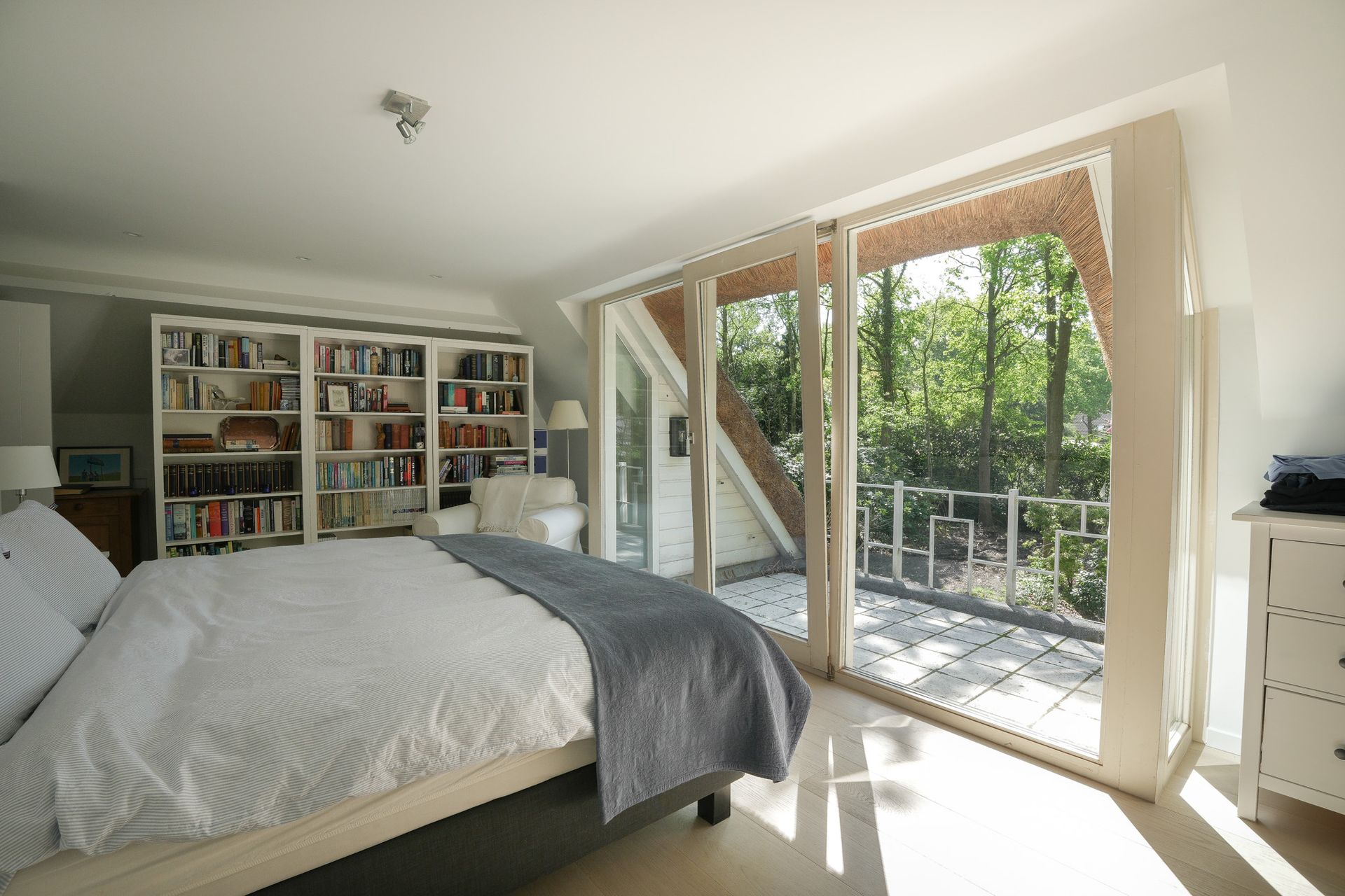 Slaapkamer met bed, ingebouwde boekenkast en balkon met uitzicht op het bos.