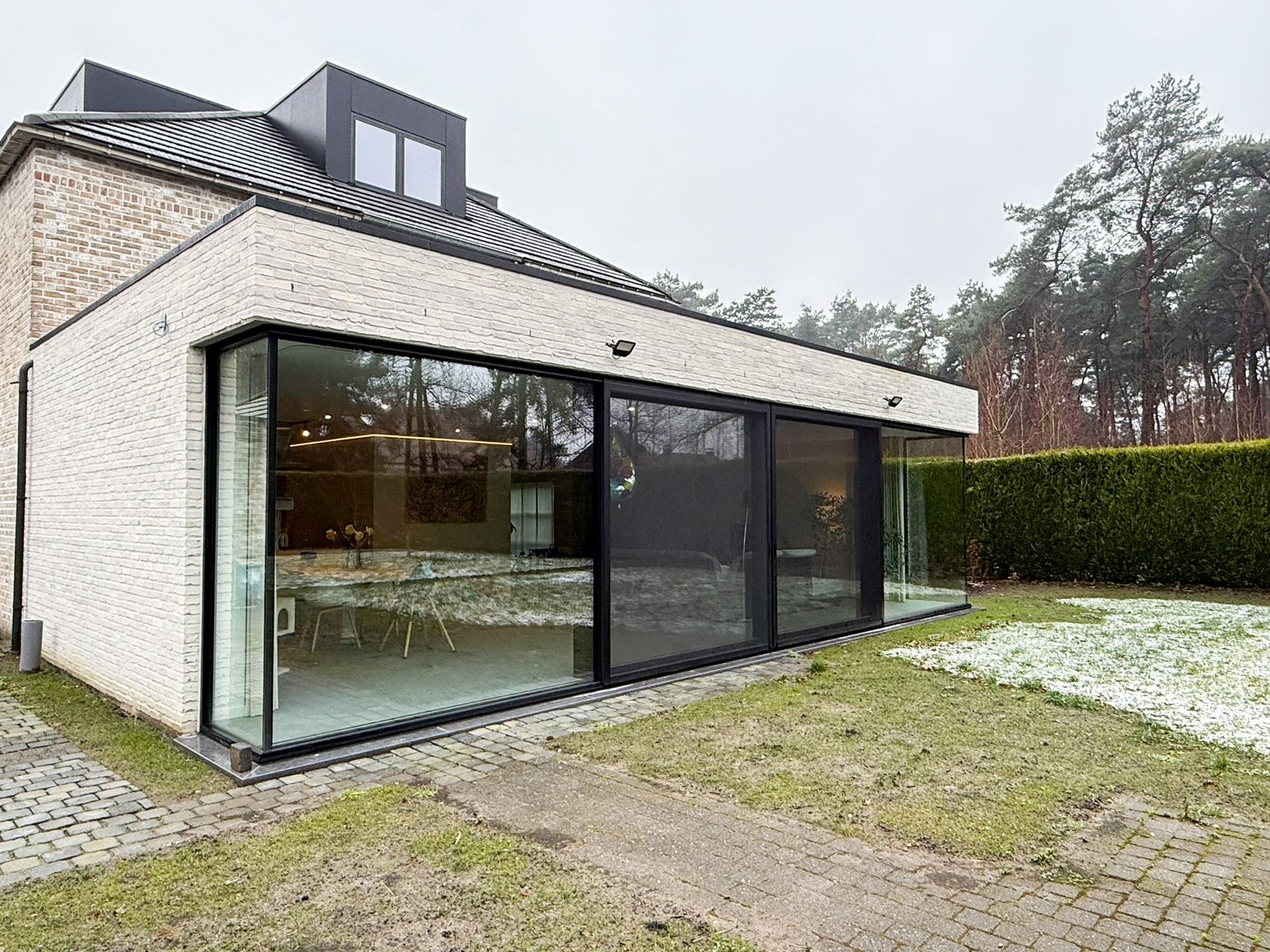 Modern huis met grote glazen ramen met uitzicht op een besneeuwde achtertuin.