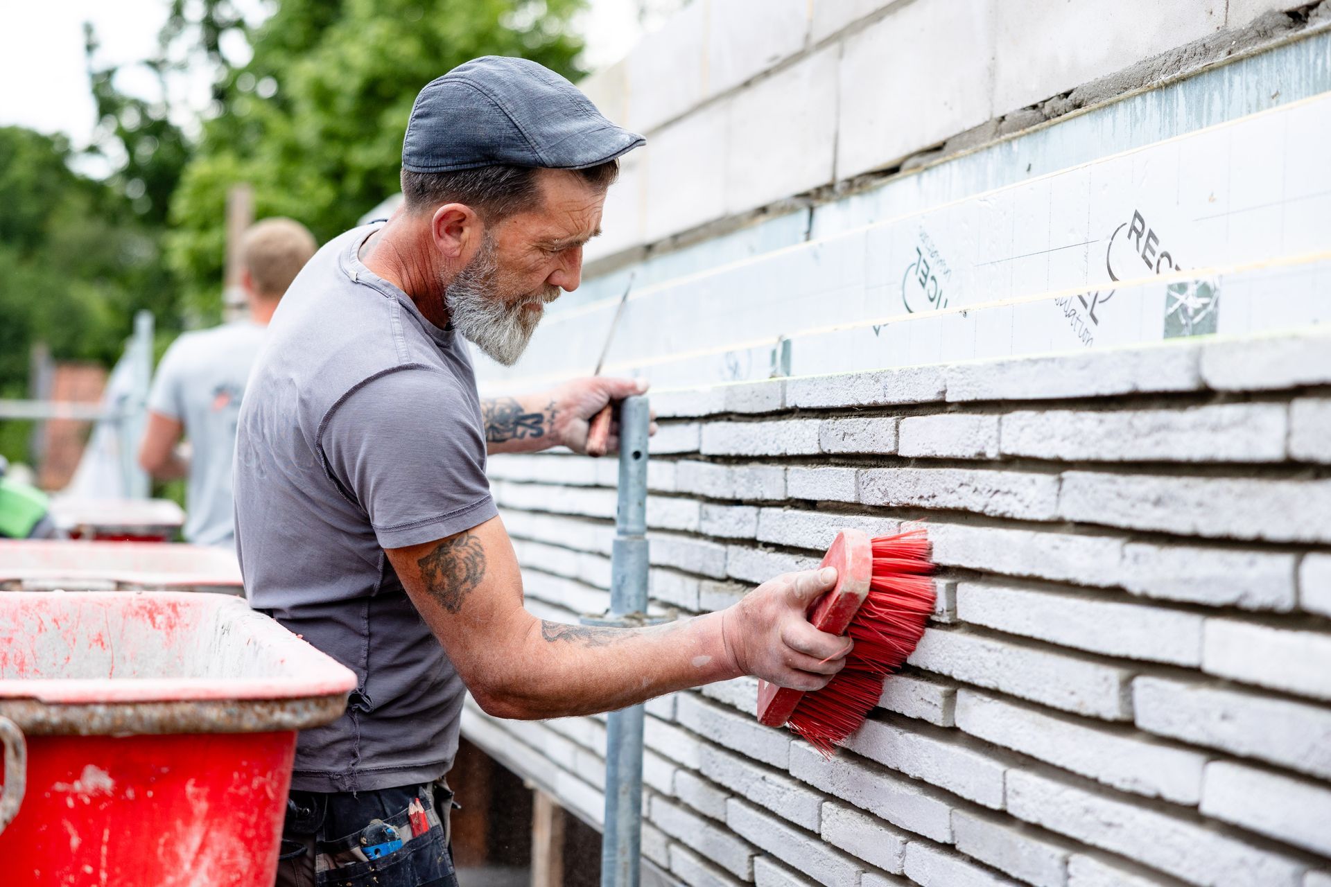 Bouwvakker gebruikt een rode borstel op witte baksteen, buiten.