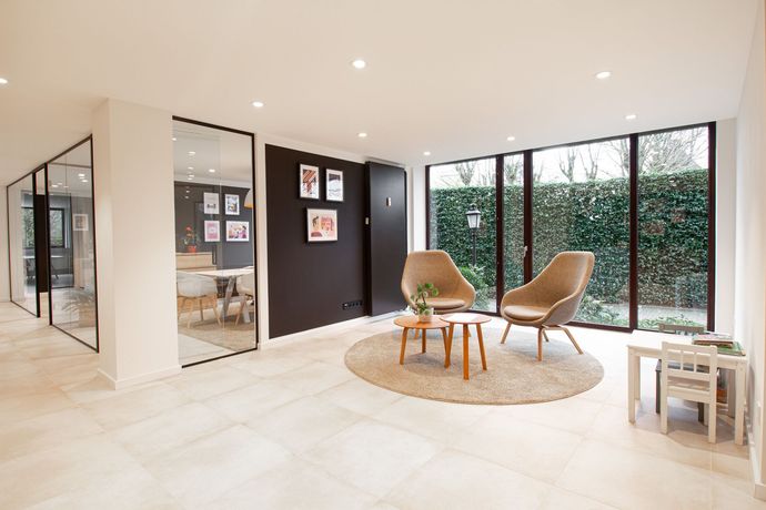 Eetkamer met houten tafel, stoelen en open zicht op de woonkamer met bank.