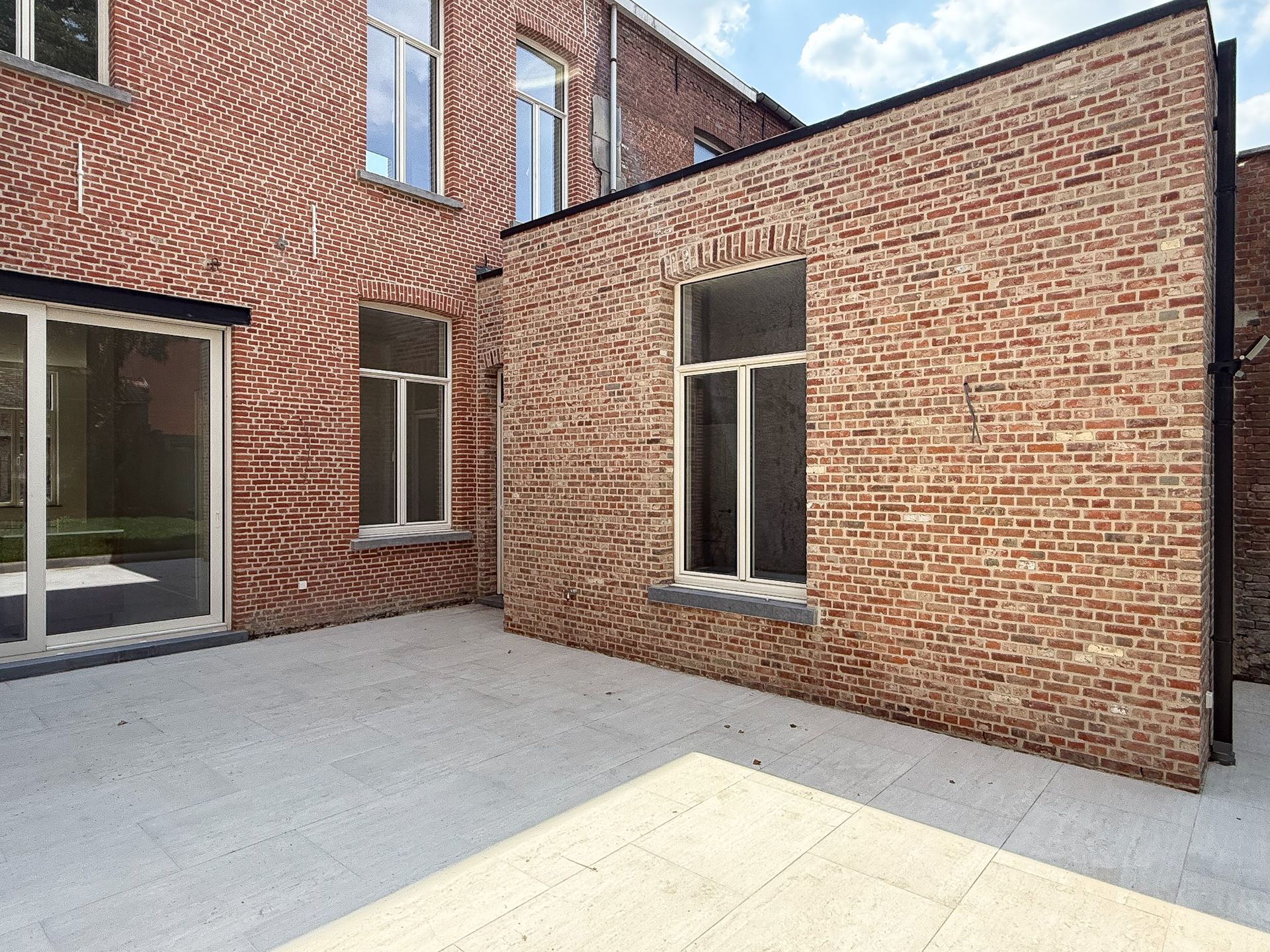 Rode bakstenen gebouwen met witte kozijnen; lichtgrijze betonnen patio; zonnige dag.