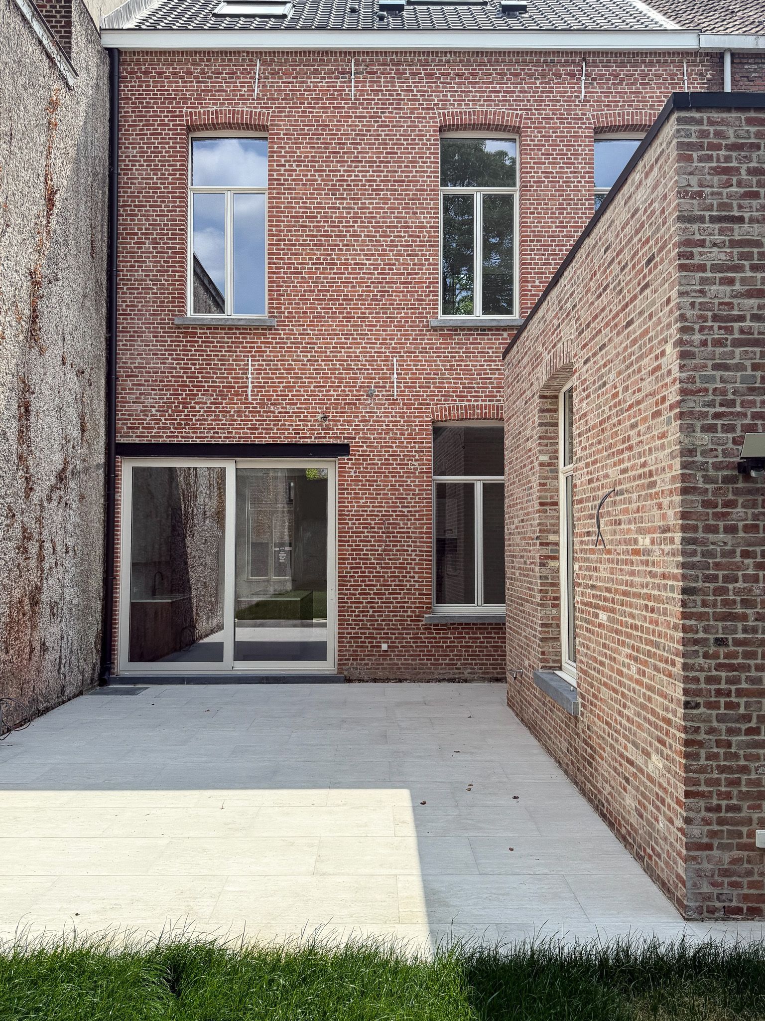 Bakstenen gebouwen met ramen en een betonnen terras. De hoofdmuur is rood met golvende patronen.