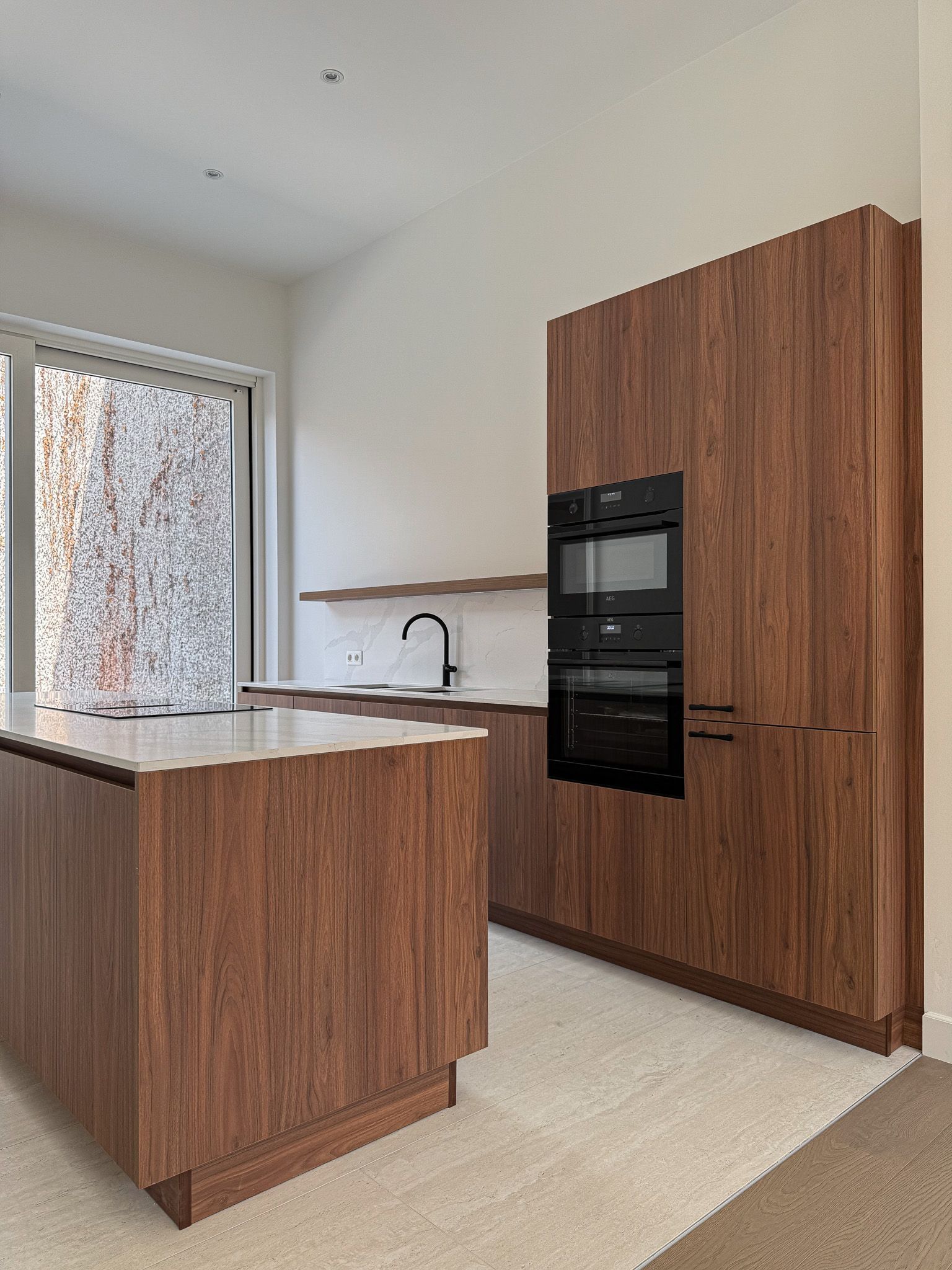 Moderne keuken met houten kasten, kookeiland, dubbele oven en raam.