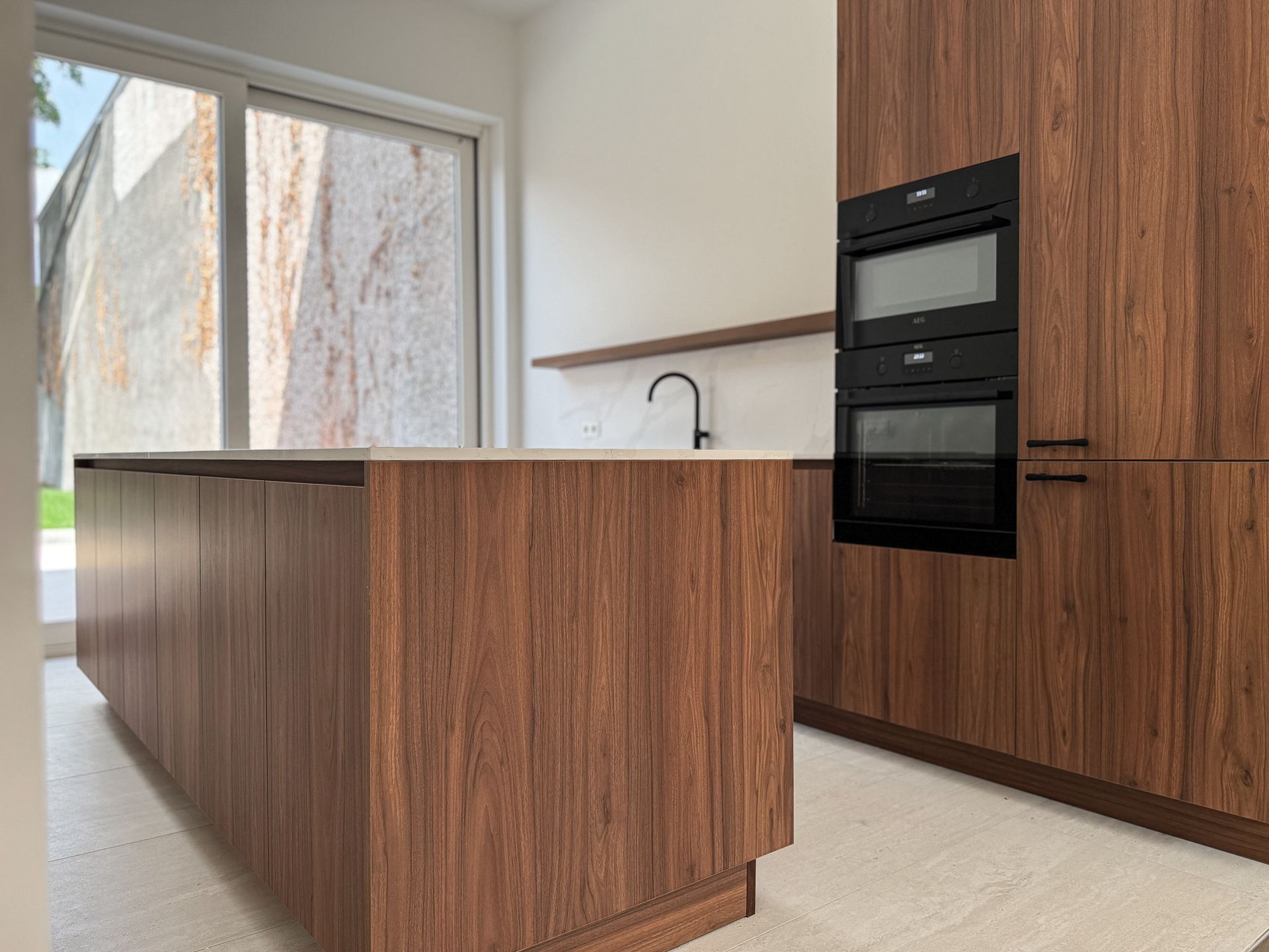 Moderne keuken met houten kasten en kookeiland. Zwarte oven en kraan. Groot raam.