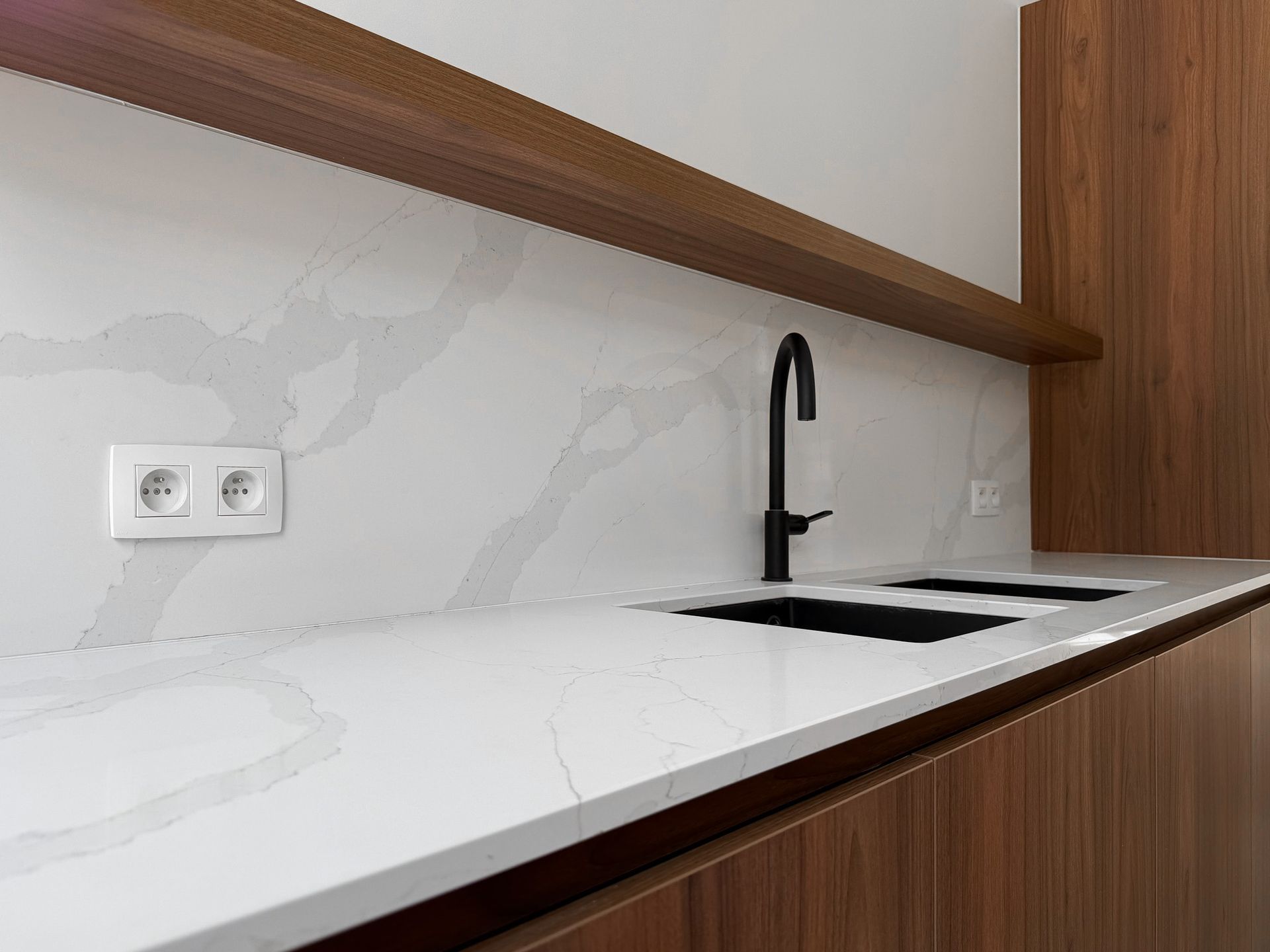Moderne keuken met wit marmeren aanrechtblad, donkere kraan en houten kasten.