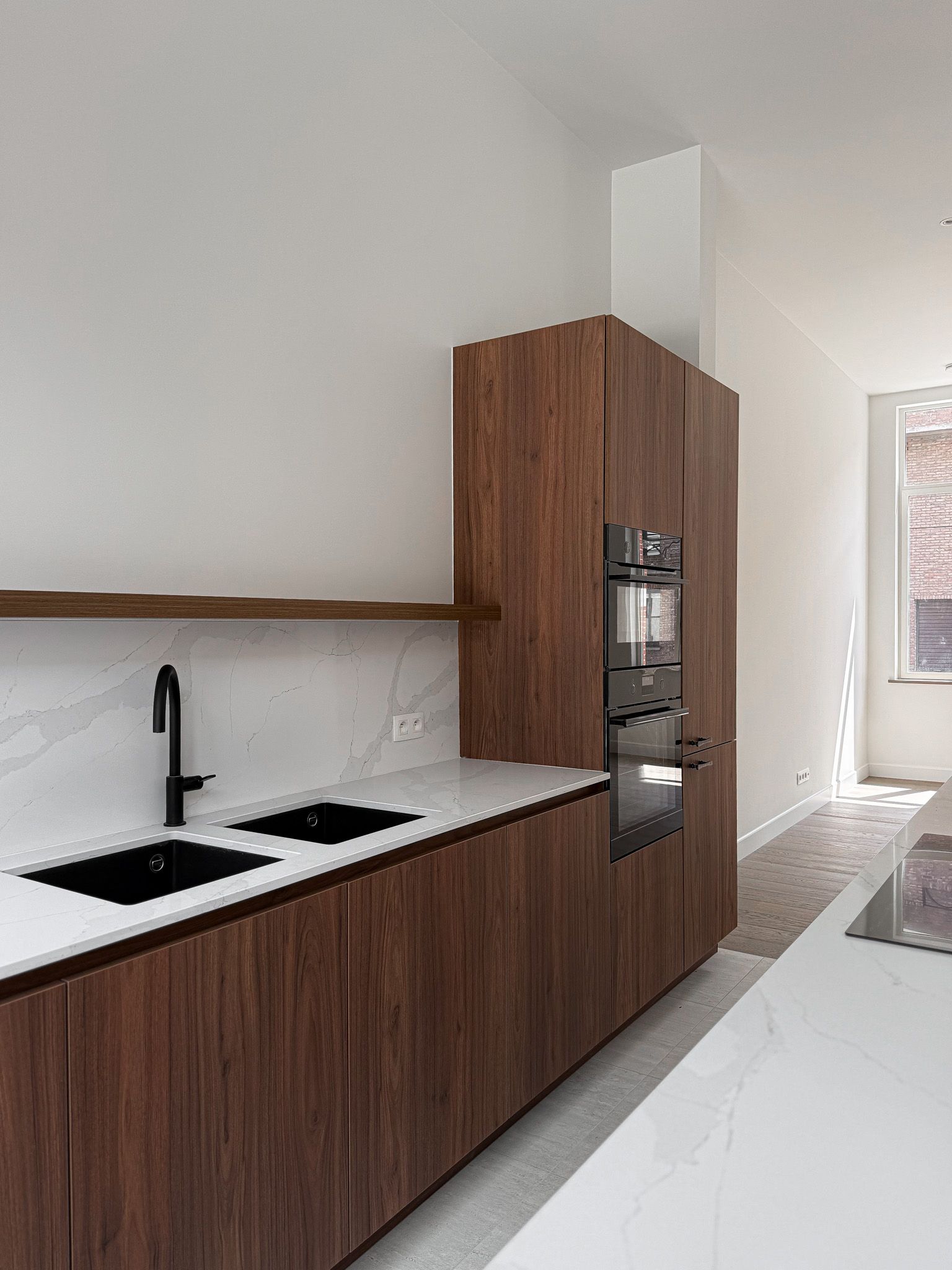 Moderne keuken met donkere houten kasten, witte aanrechtbladen en een zwarte kraan en spoelbak.