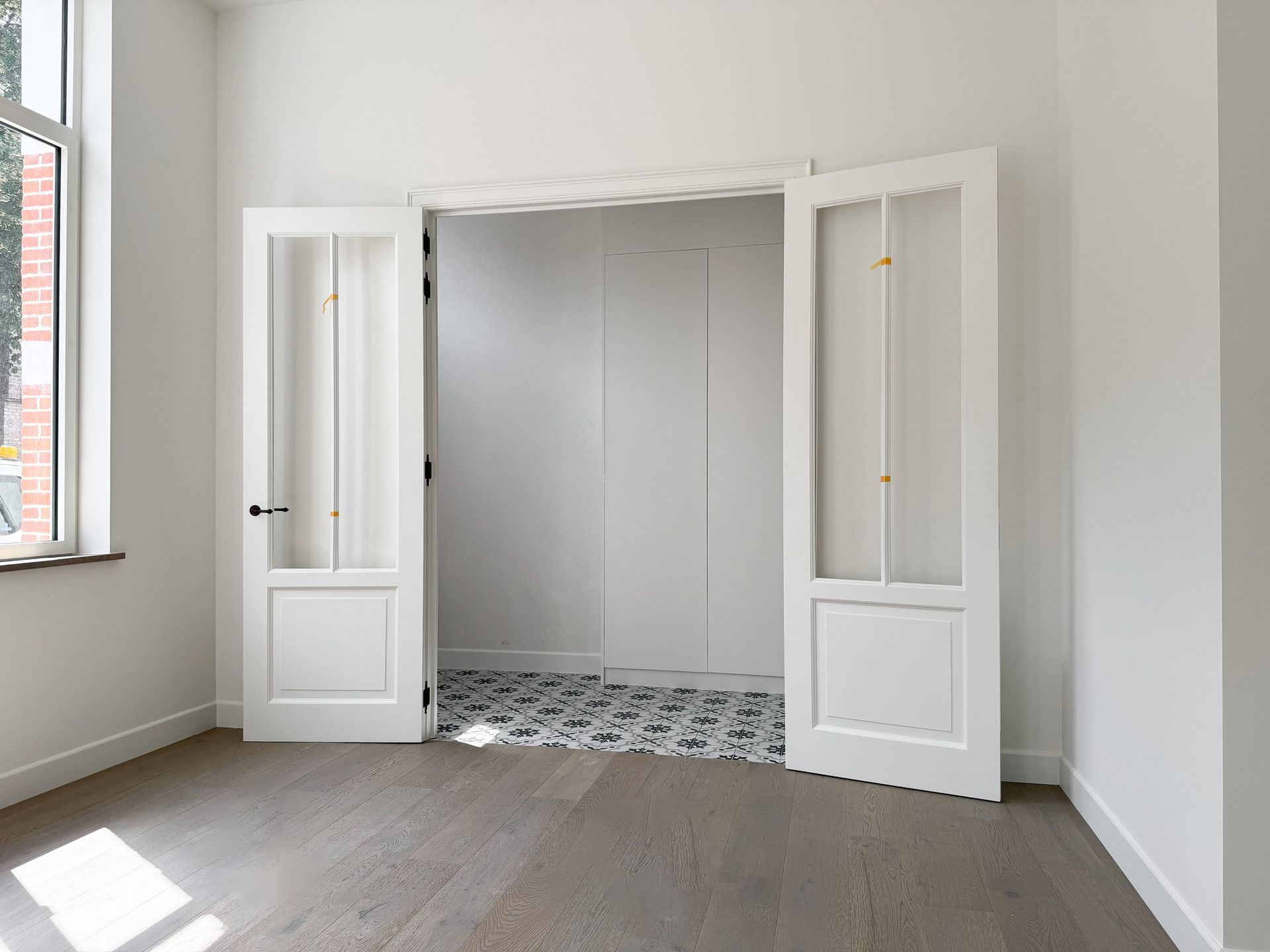 Witte binnendeuren geven toegang tot een kleine kamer met een tegelvloer met patroon. Lichte, strakke ruimte met houten vloeren.