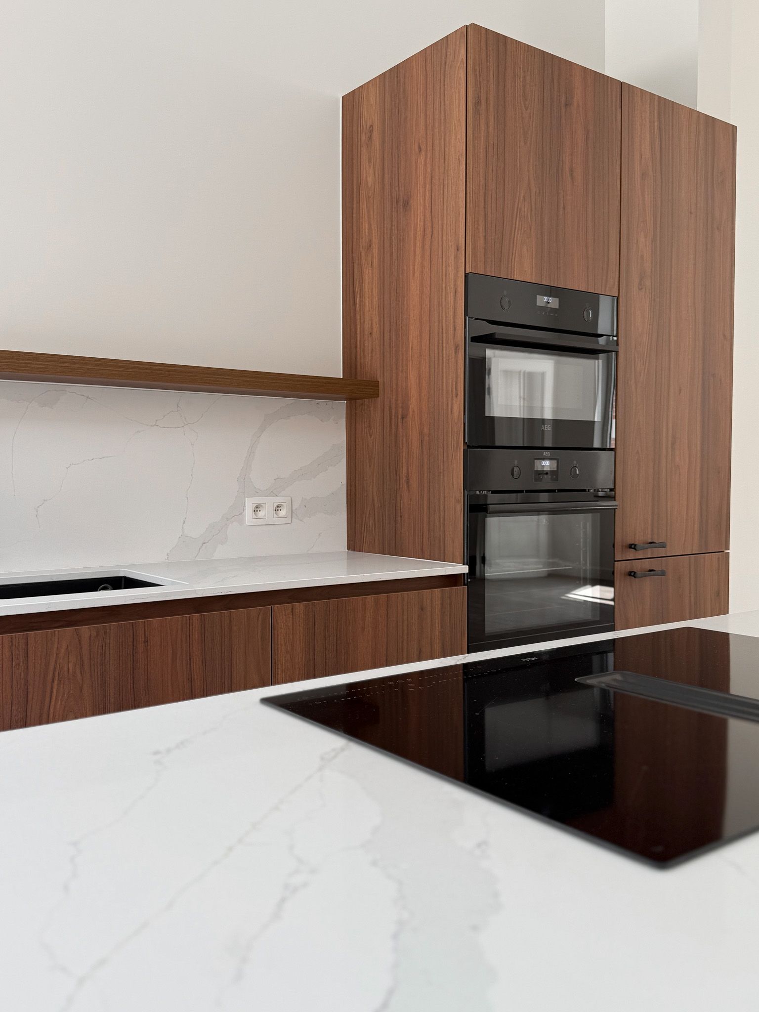 Moderne keuken met houten kasten en ingebouwde zwarte ovens. Wit aanrechtblad en kookplaat.