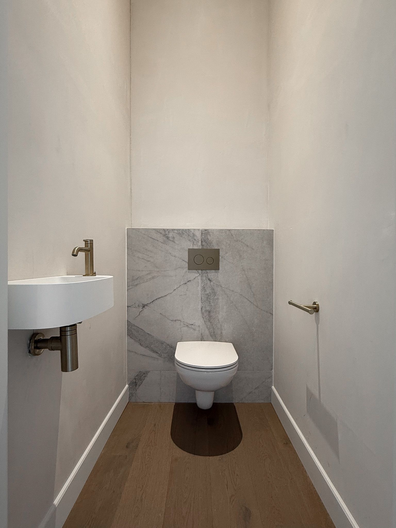 Kleine, moderne badkamer met witte muren, houten vloer, marmeraccenten en toilet.