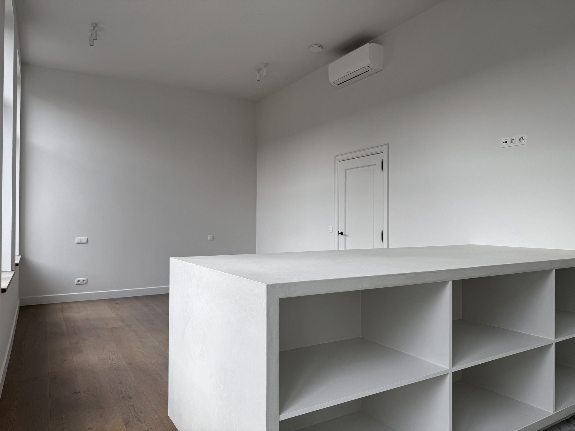 Lege witte kamer met groot kookeiland en houten vloer.