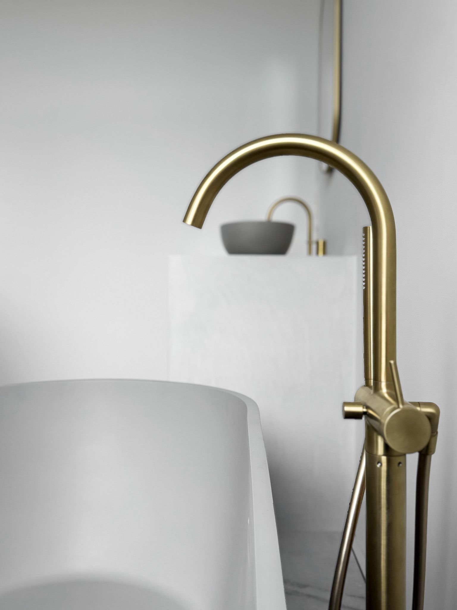Vrijstaande gouden badkraan, wit bad en kleine wastafel in een moderne badkamer.
